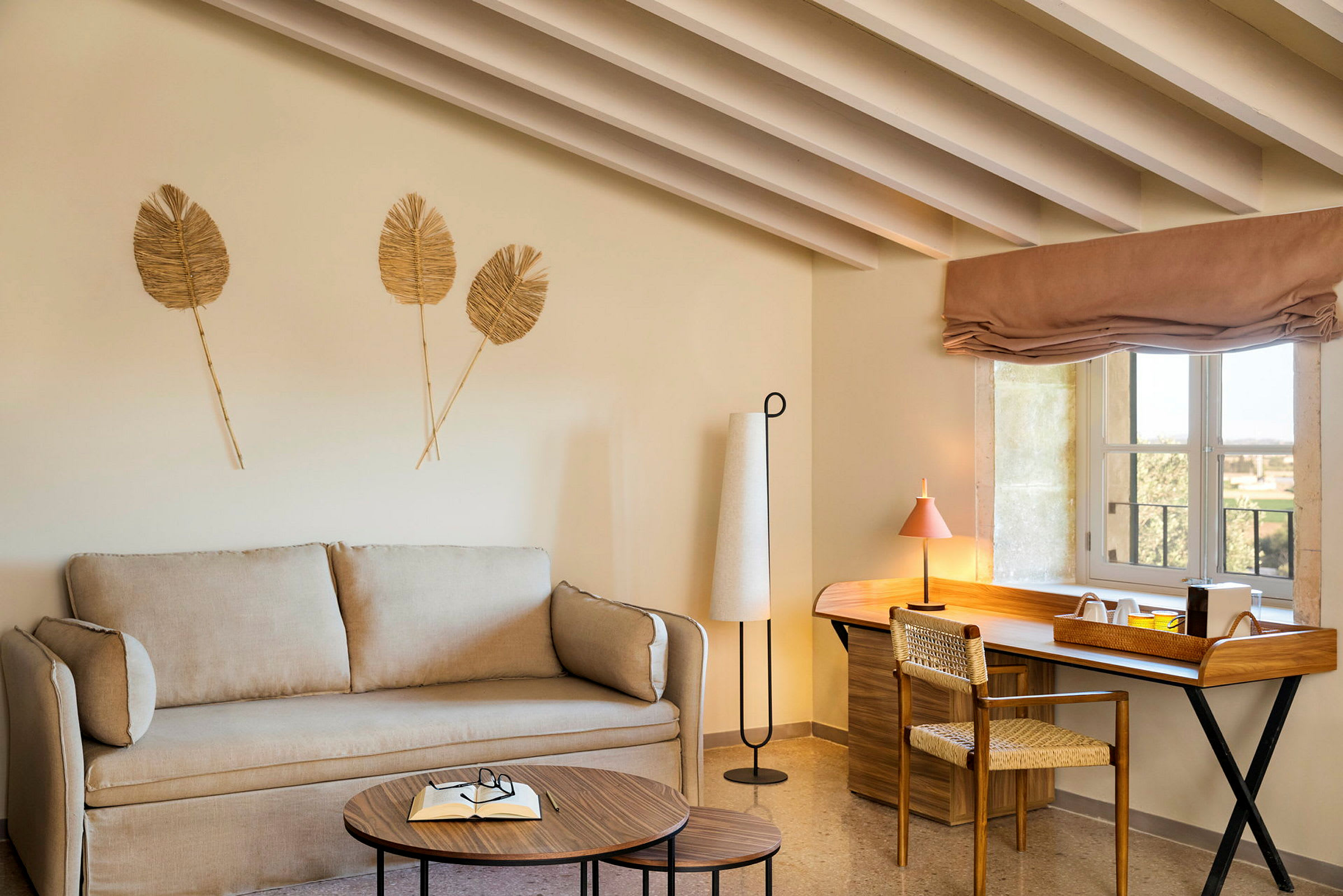 Ett rum med en beige soffa, träbord och en skrivbordsplats med fönster. (AI-genererad text)