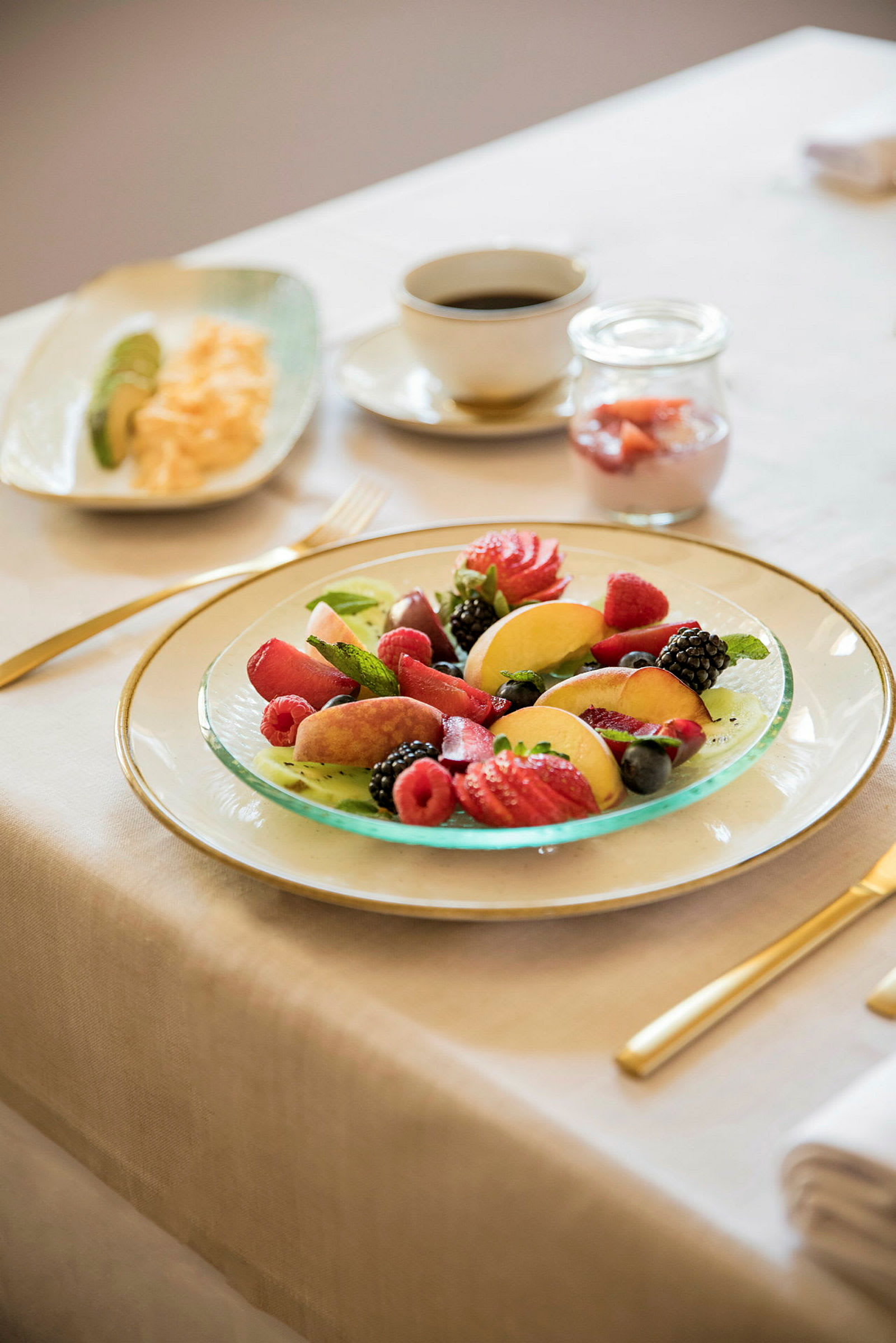 Ett bord med en frukostservering inklusive en fruktsallad, ägg, avokado, yoghurt och kaffe. (AI-genererad text)
