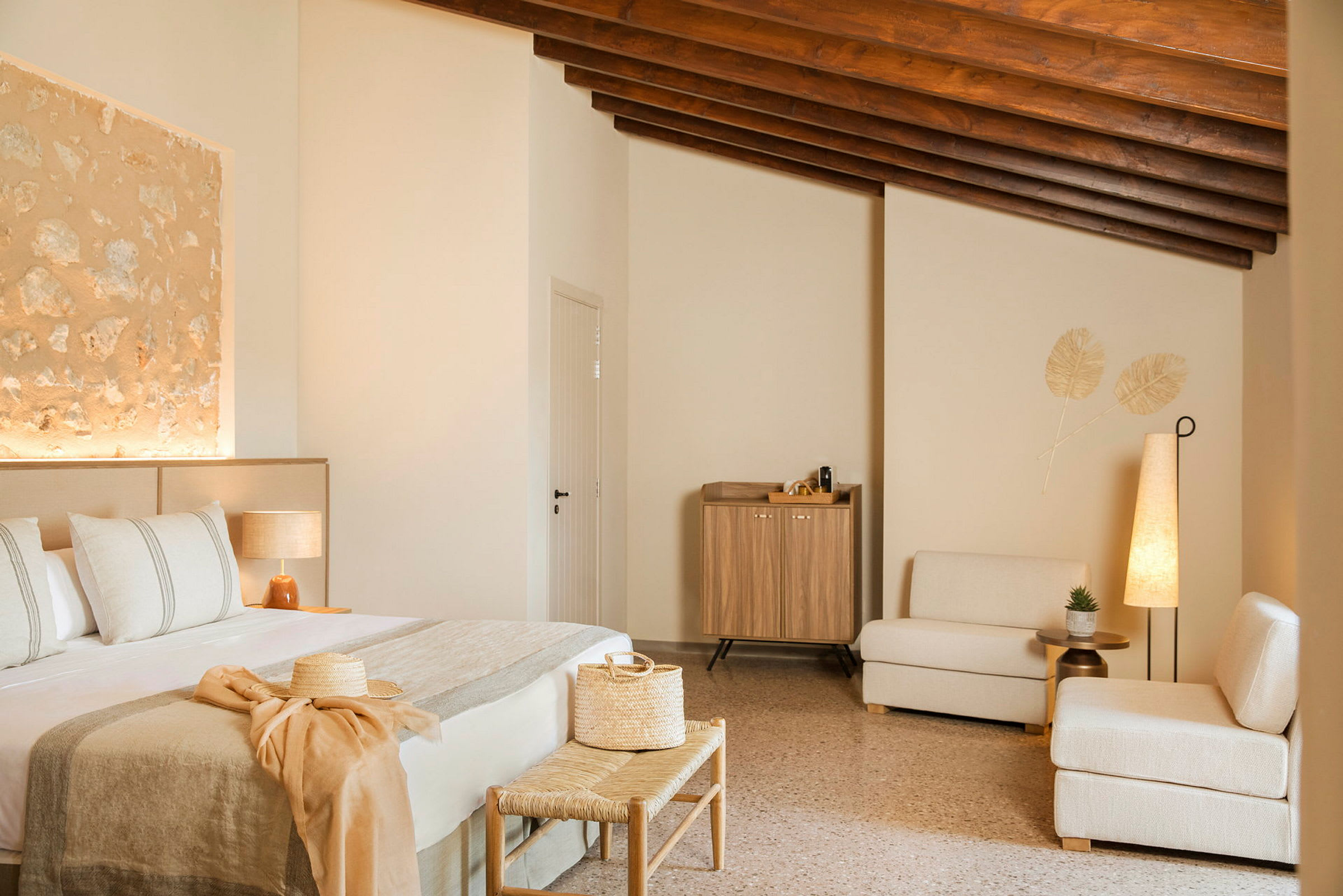 Ett inrett hotellrum med en säng, sittmöbler och ett skåp. Rummet har en varm, modern stil med beige och naturliga trädetaljer. (AI-genererad text)