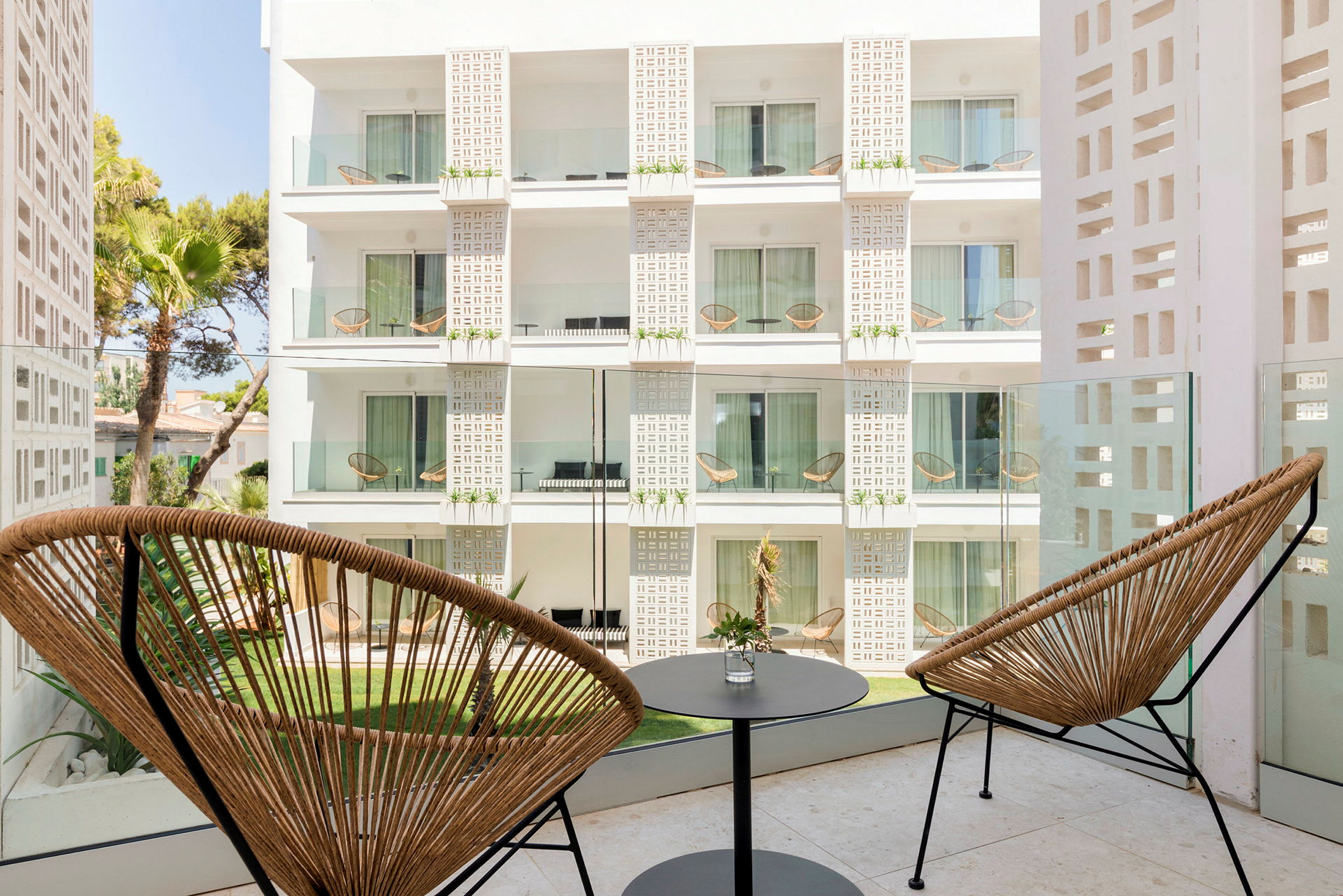Hotellbalkong med två stolar och ett litet bord med utsikt mot en byggnads fasad. (AI-genererad text)