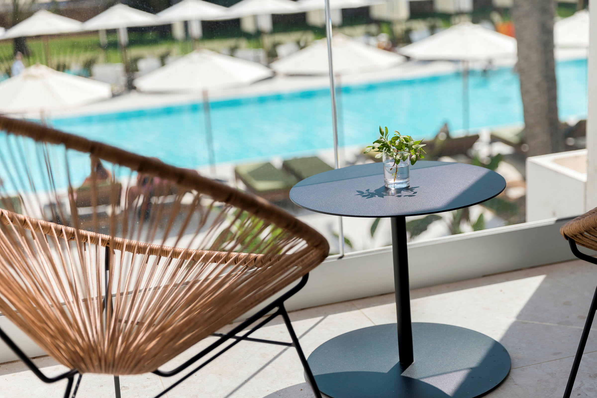 En sittgrupp med ett bord och stolar framför ett fönster med utsikt över en pool och solstolar. (AI-genererad text)