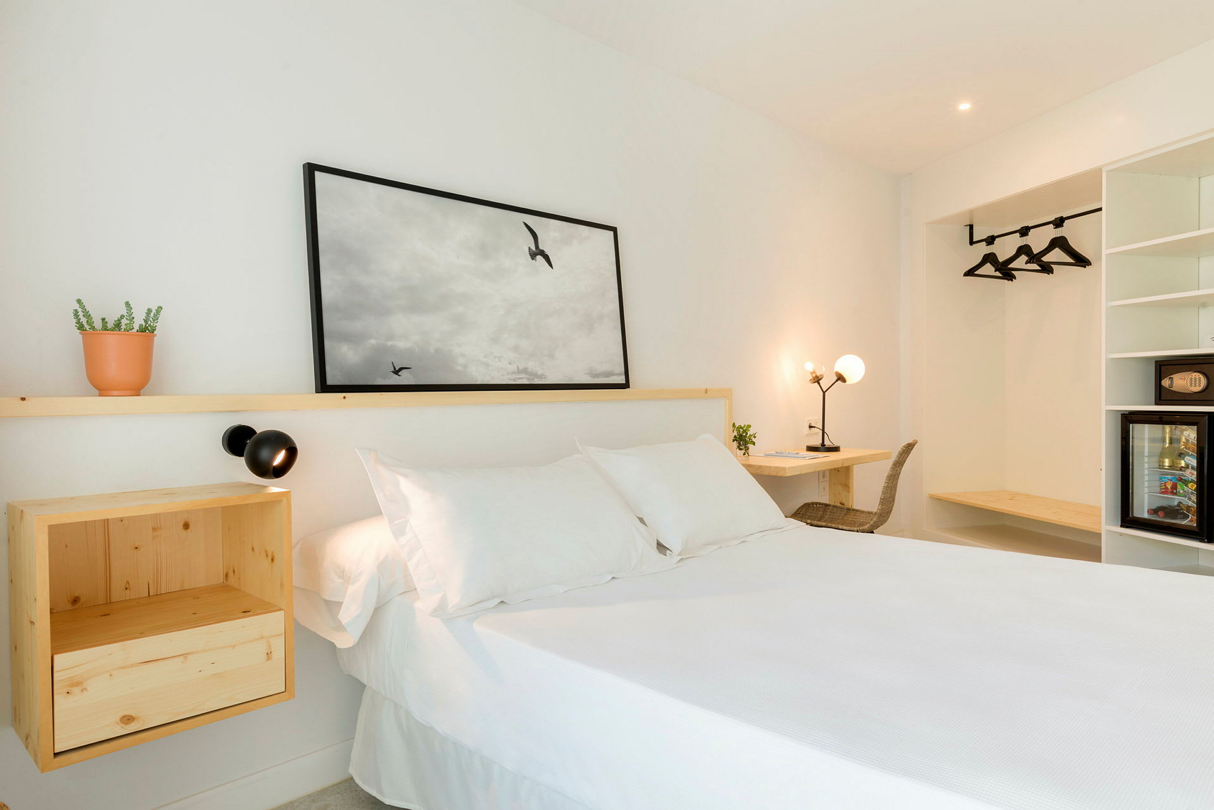 En ljus hotellrum med en vit säng, trämöbler och väggdekoration. (AI-genererad text)