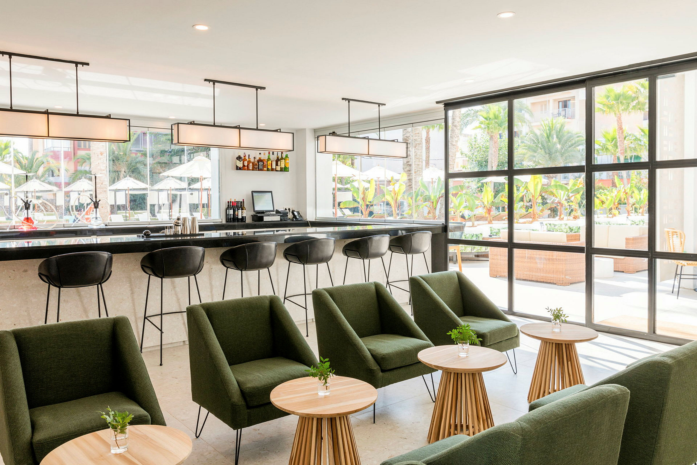 Modern bar med stolar och grön sittgrupp framför stora fönster som vetter mot en utomhusterrass. (AI-genererad text)