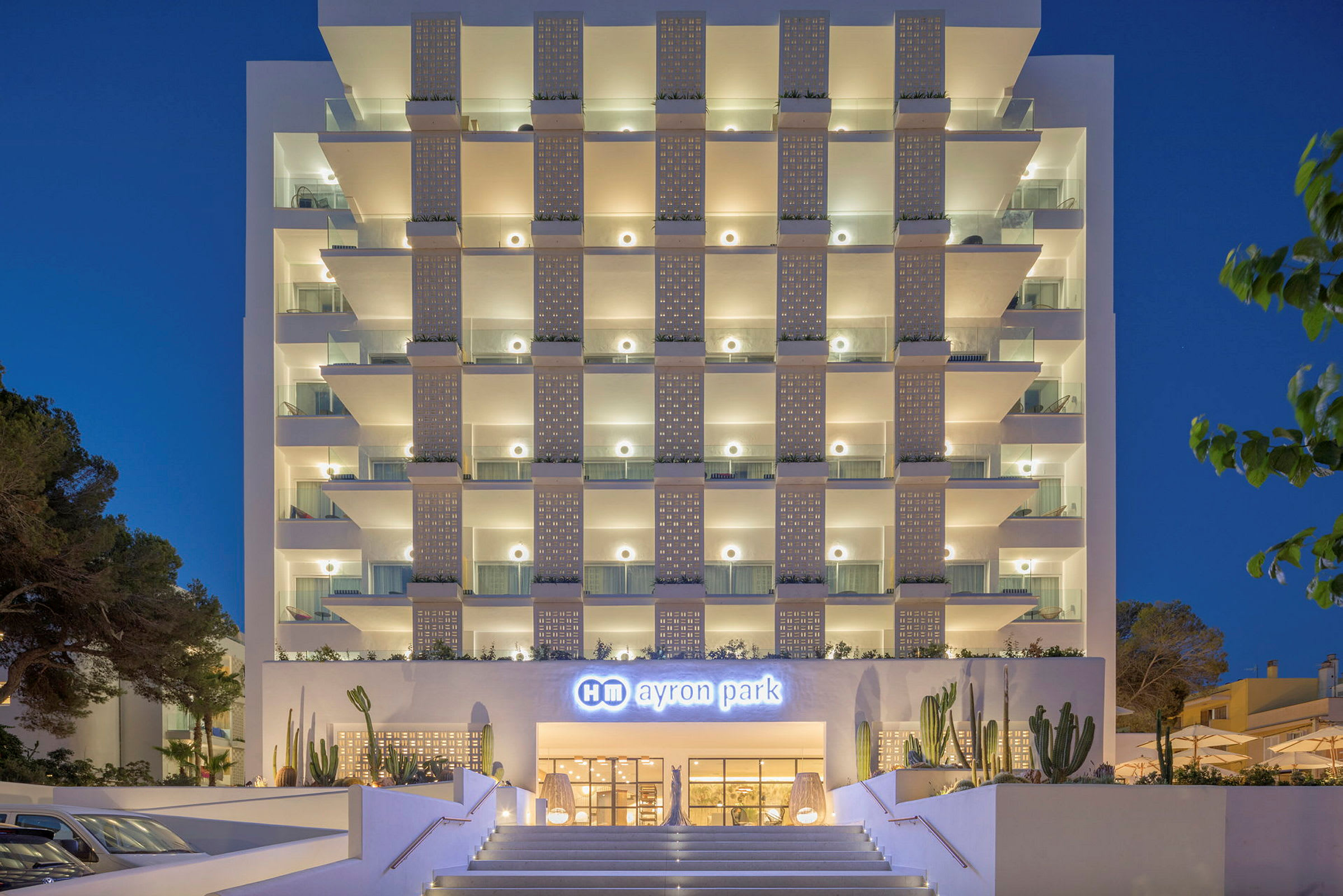 Hotell Ayron Parks fasad vid kvällstid med upplysta balkonger och huvudentré. (AI-genererad text)