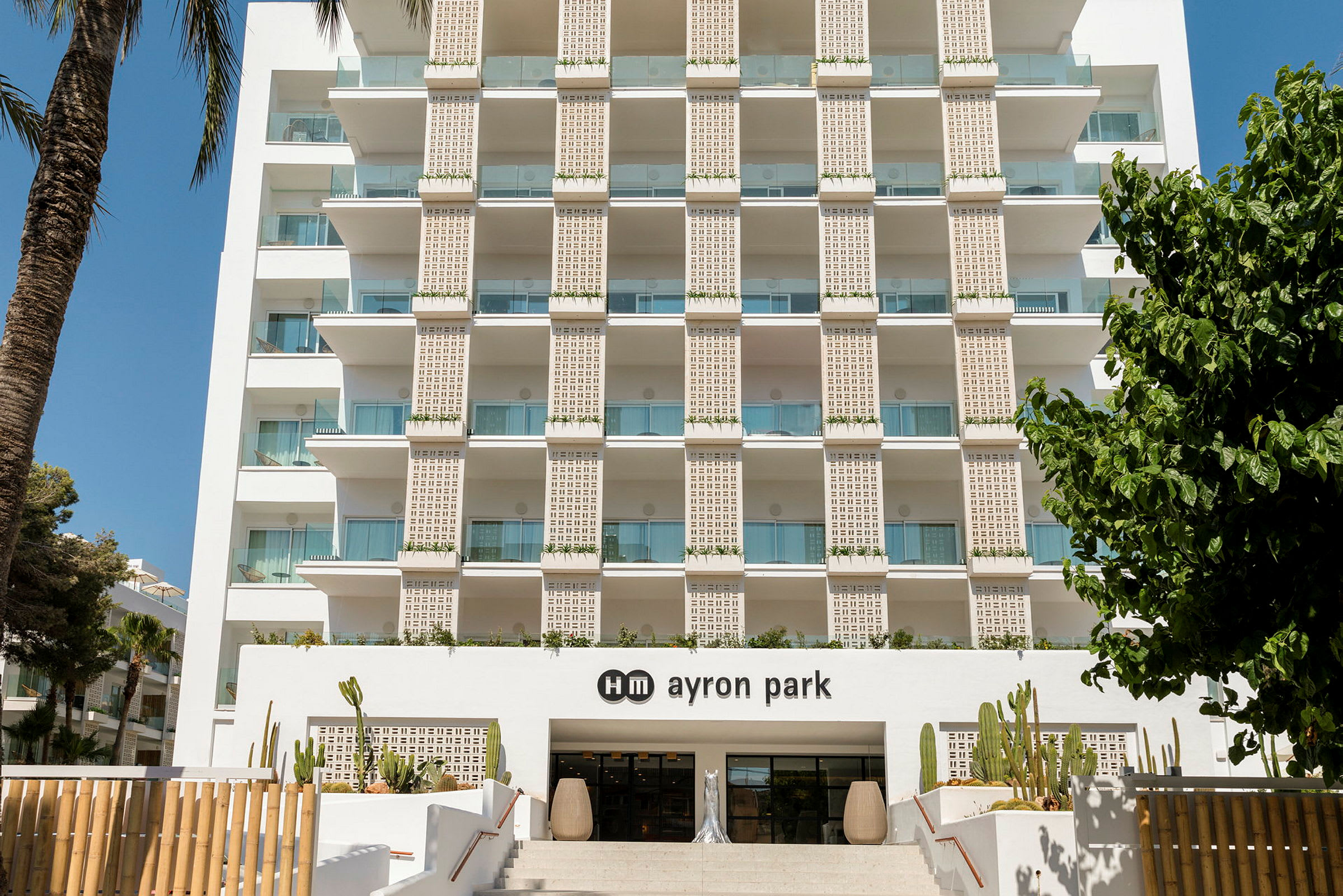Hotellfasaden med balkonger och entrén till hm ayron park, dekorerad med kaktusar. (AI-genererad text)