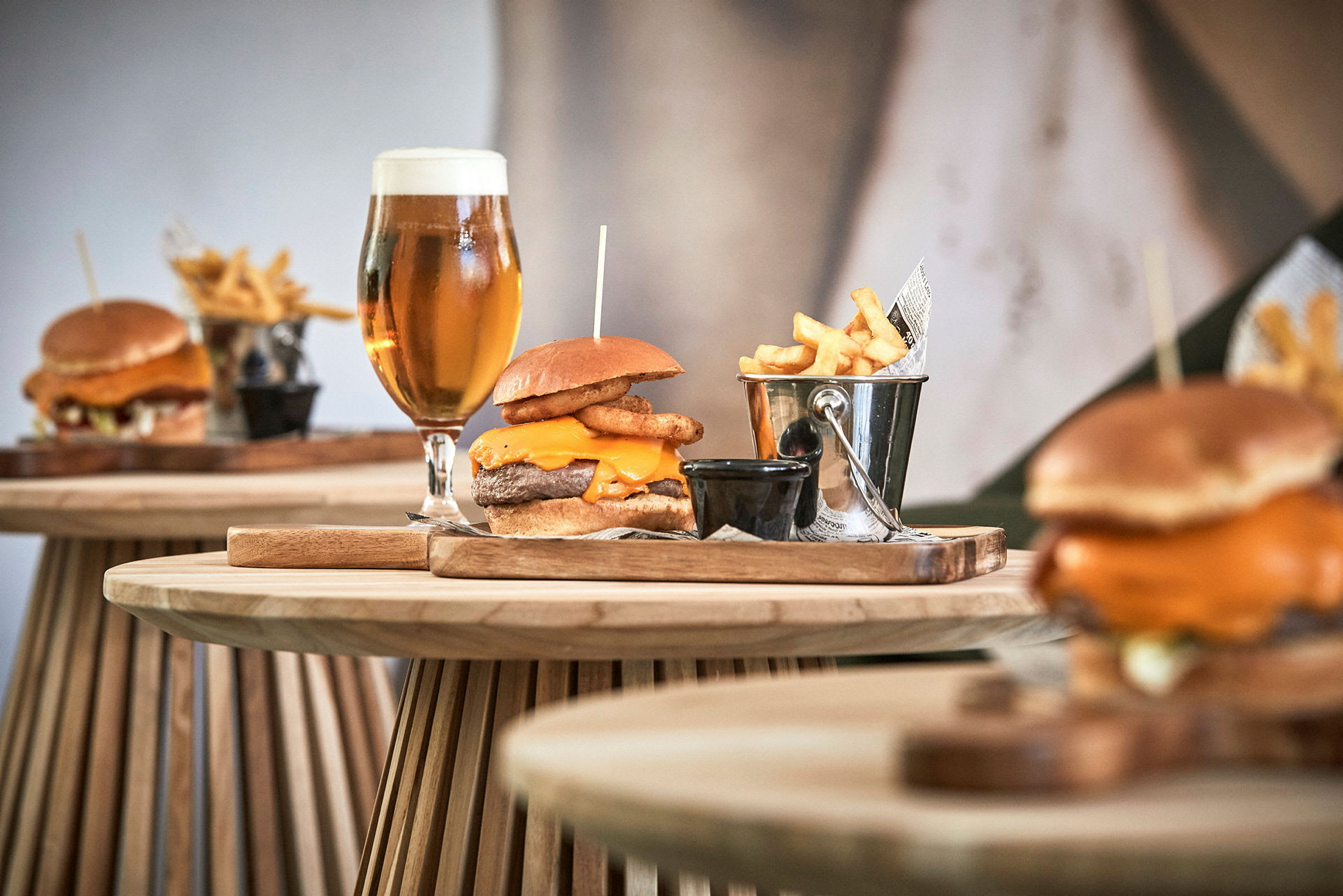 Tallrikar med hamburgare, pommes frites i metallhink och glas med öl på träbord. (AI-genererad text)