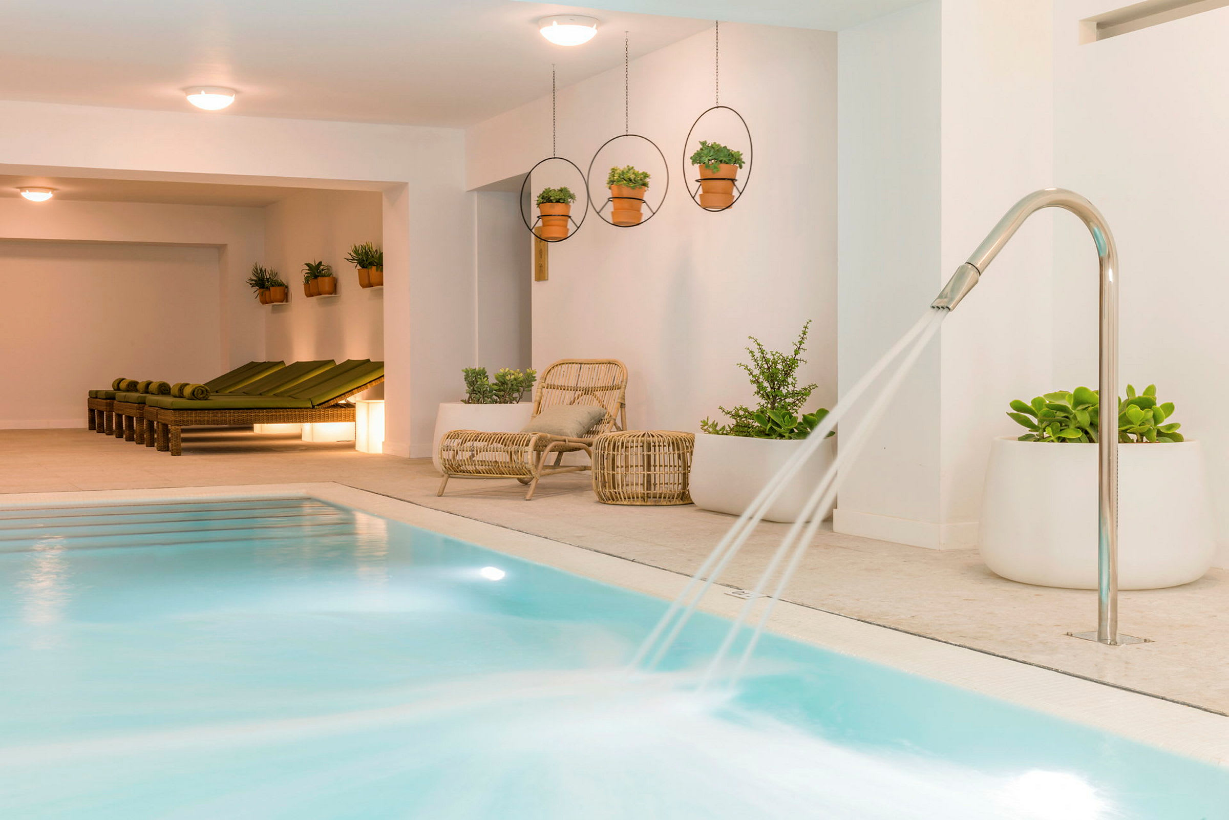 Inomhuspool med vattenstrålar och vilstolar bredvid växter. (AI-genererad text)