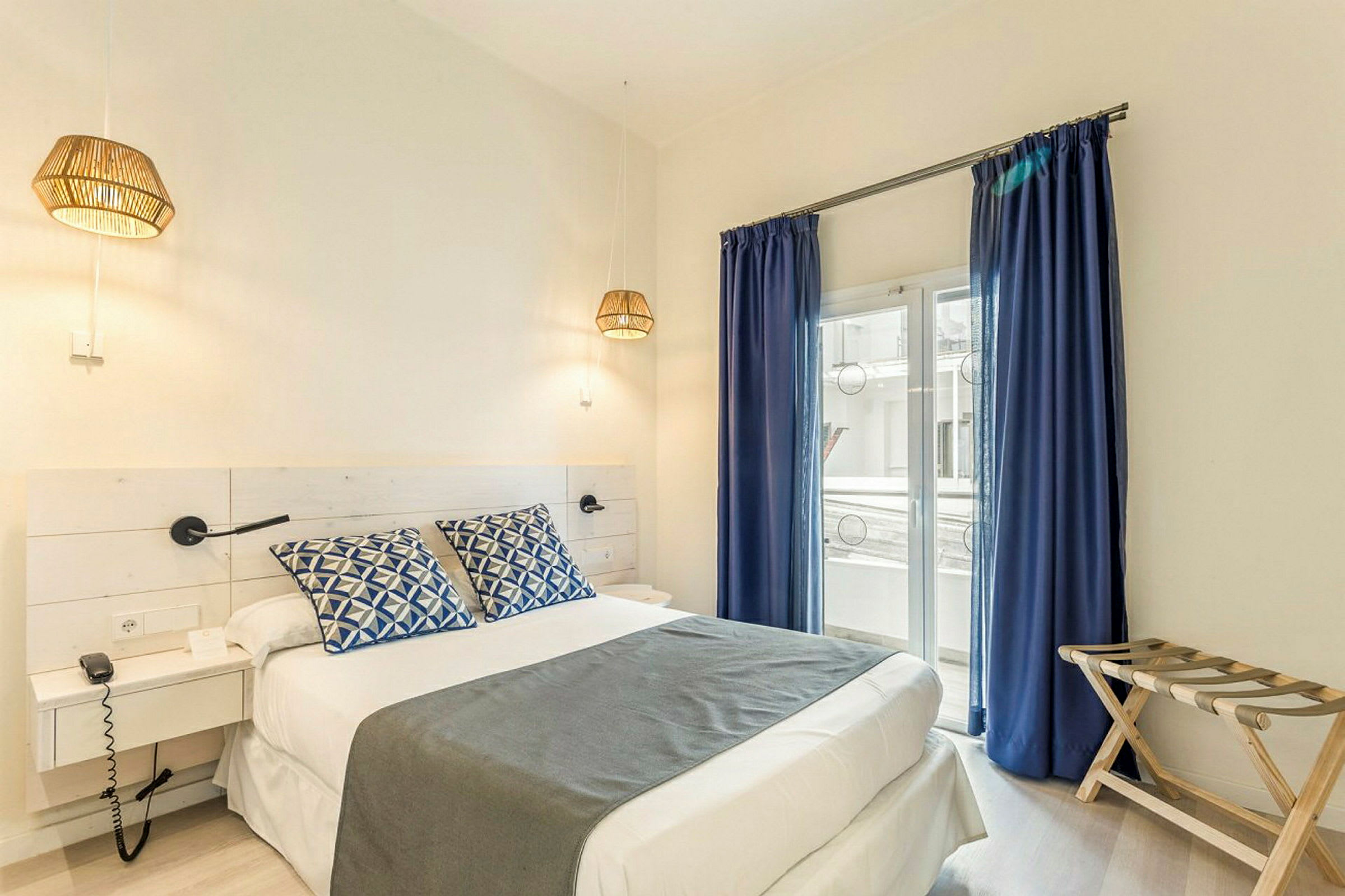 Ett hotellrum med en dubbelsäng, blå gardiner och fönster mot en balkong. (AI-genererad text)
