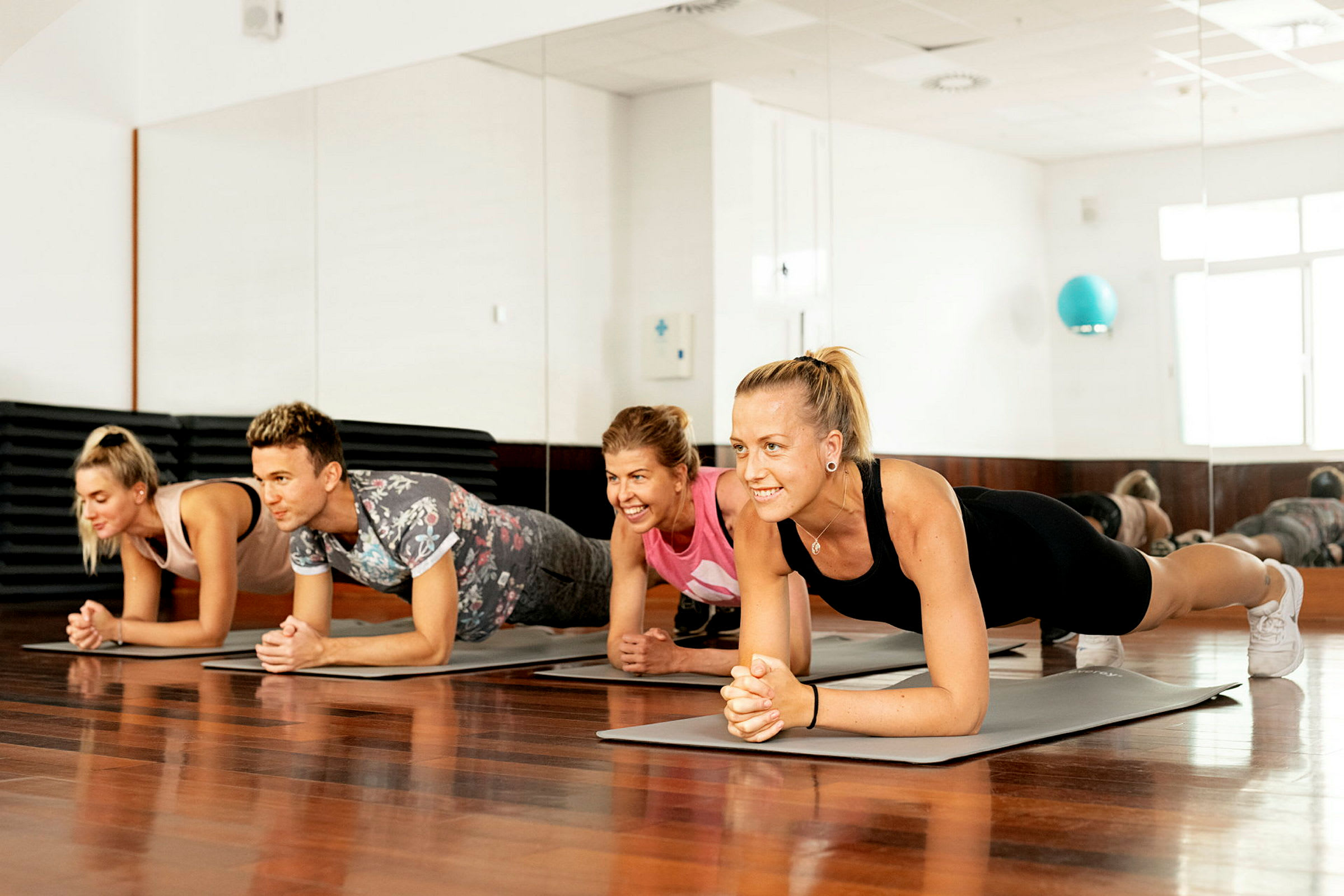 Personer utövar plankövningar på yogamattor i ett ljust rum med spegelvägg. (AI-genererad text)