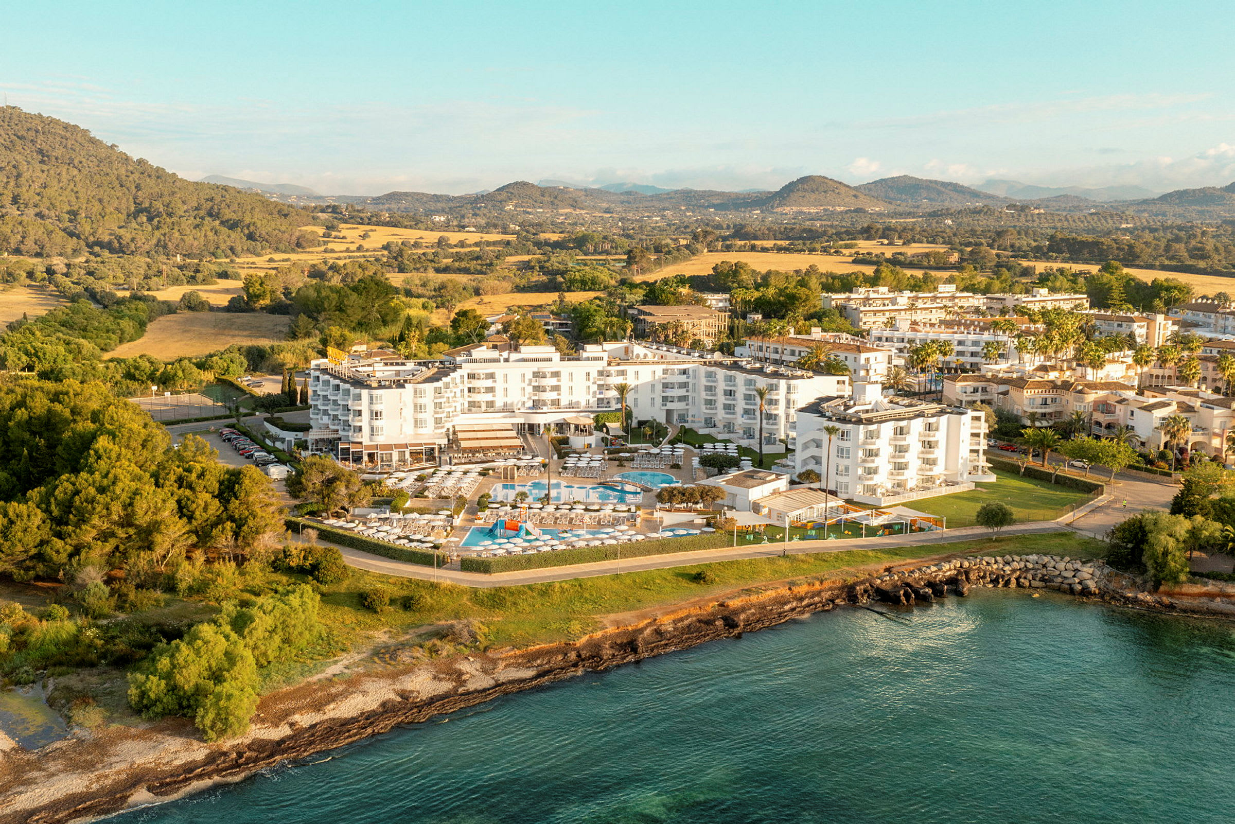 Flygbild över ett hotellkomplex omgivet av grönska och vattnet. (AI-genererad text)