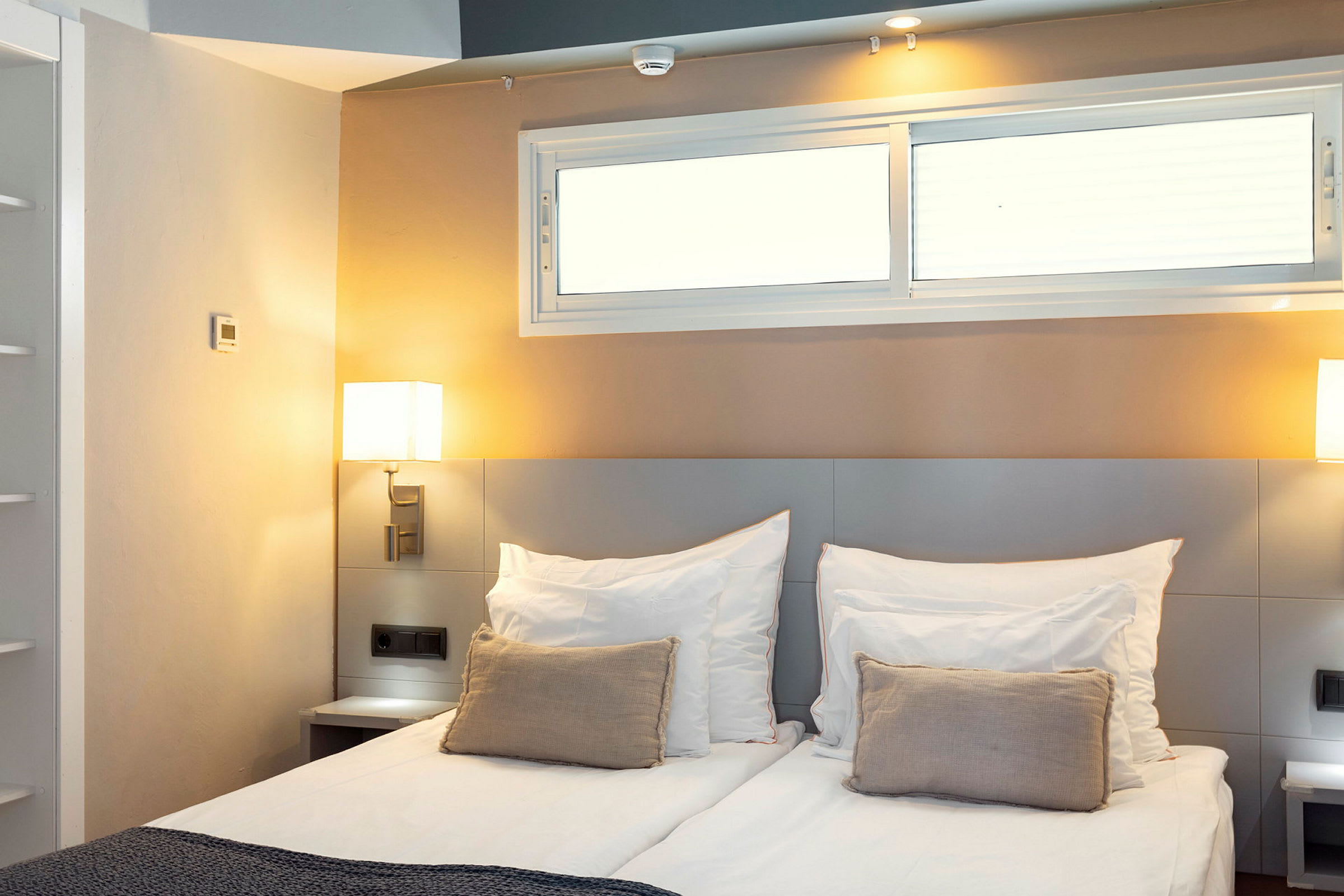 Ett hotellrum med en dubbelsäng, dekorativ kudde och sänglampor bredvid. (AI-genererad text)