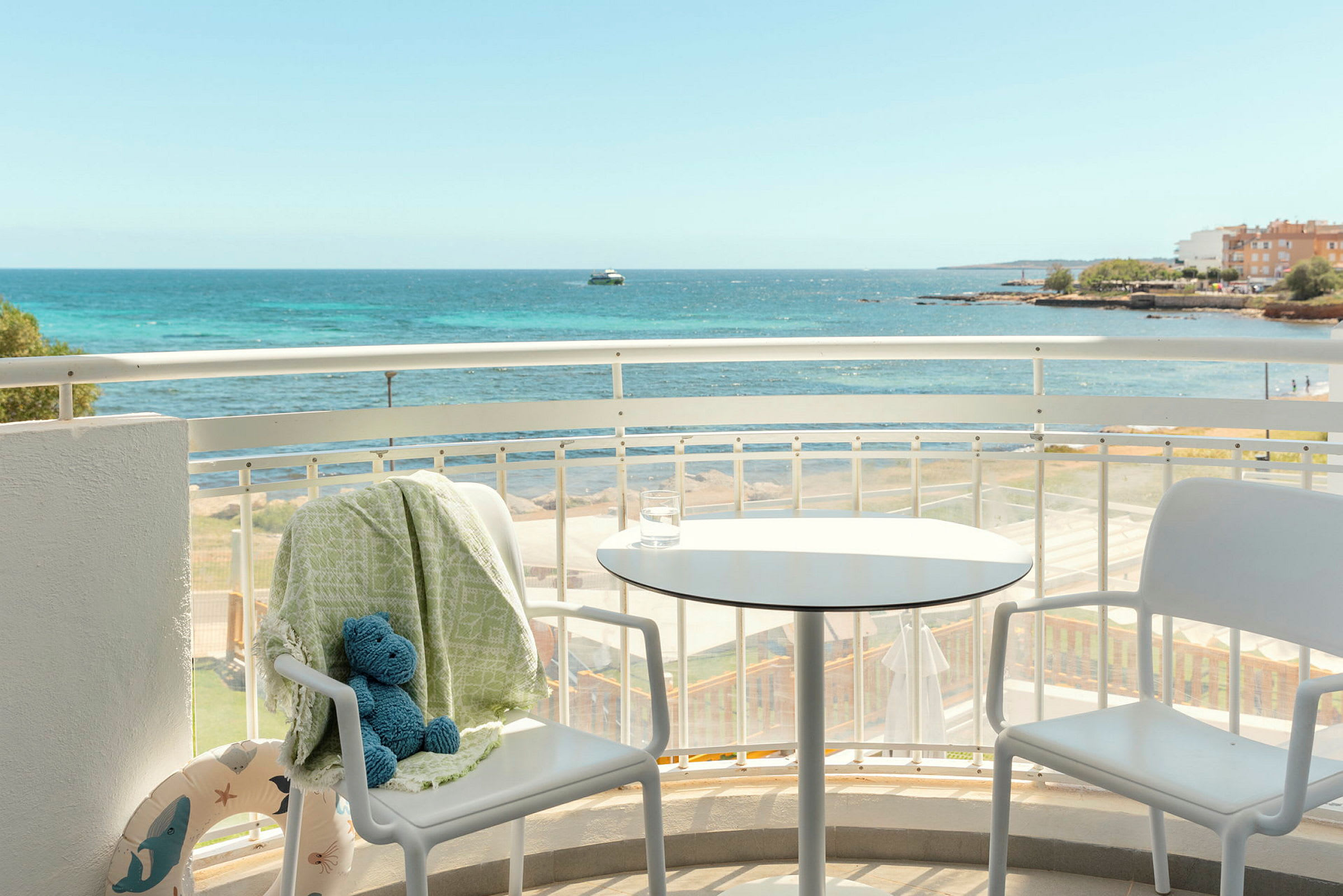 En balkong med två vita stolar och ett bord, med utsikt över havet. (AI-genererad text)