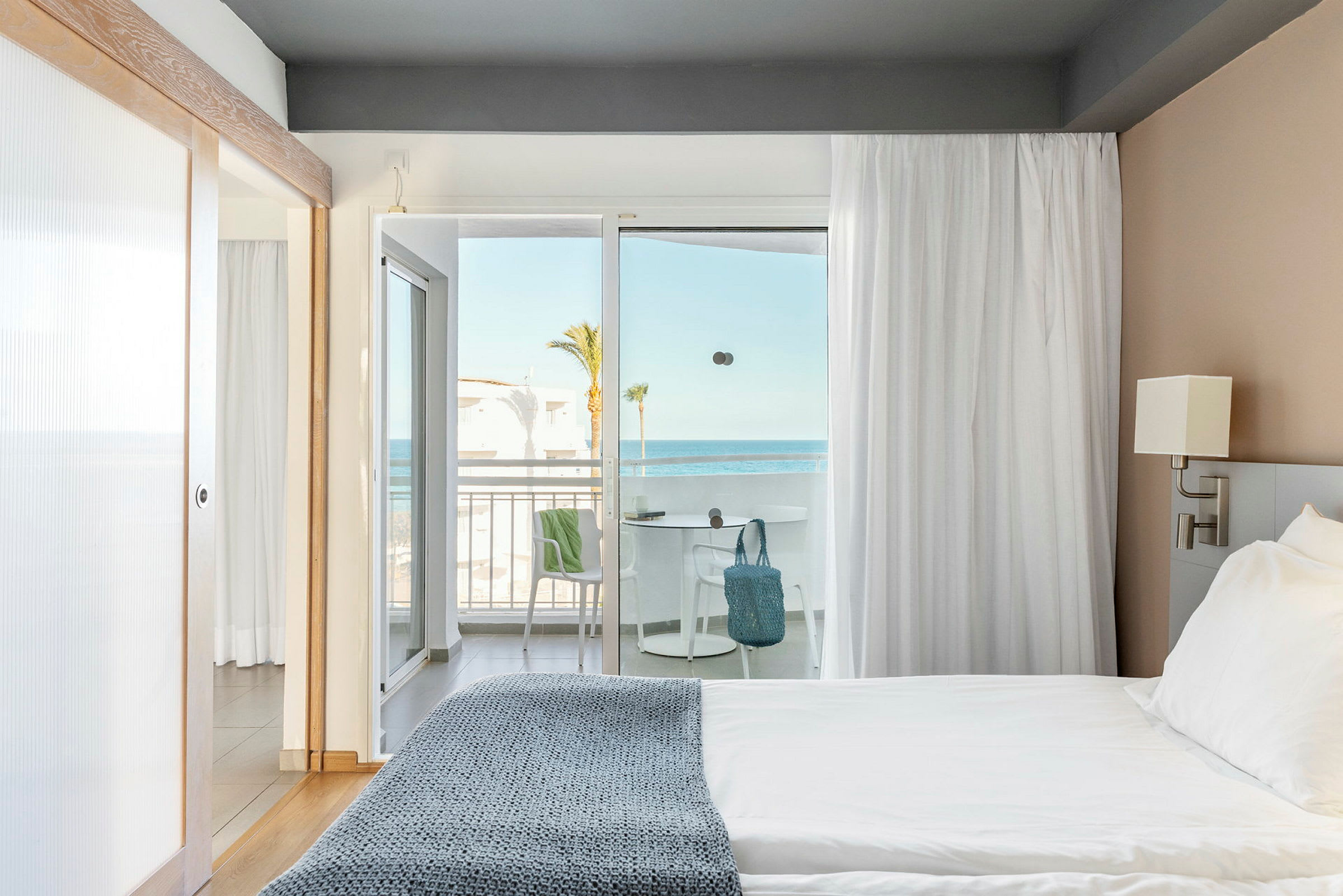 Hotellrum med säng nära ett ljusinsläpp mot en balkong med havsutsikt. (AI-genererad text)