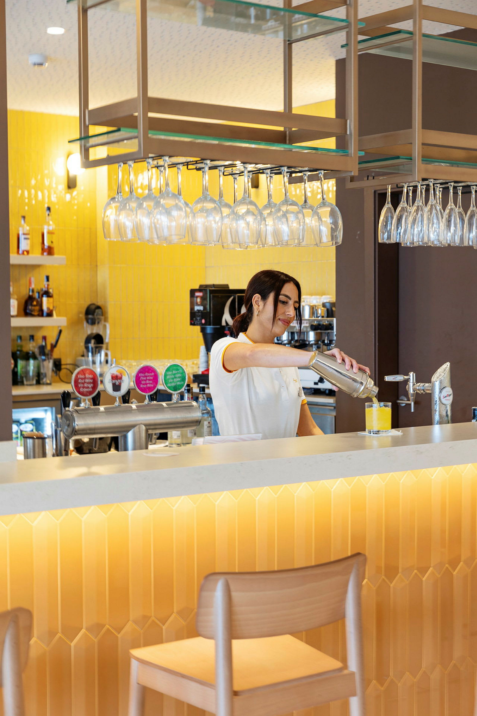 Person förbereder en drink vid en bar med gul inredning. (AI-genererad text)
