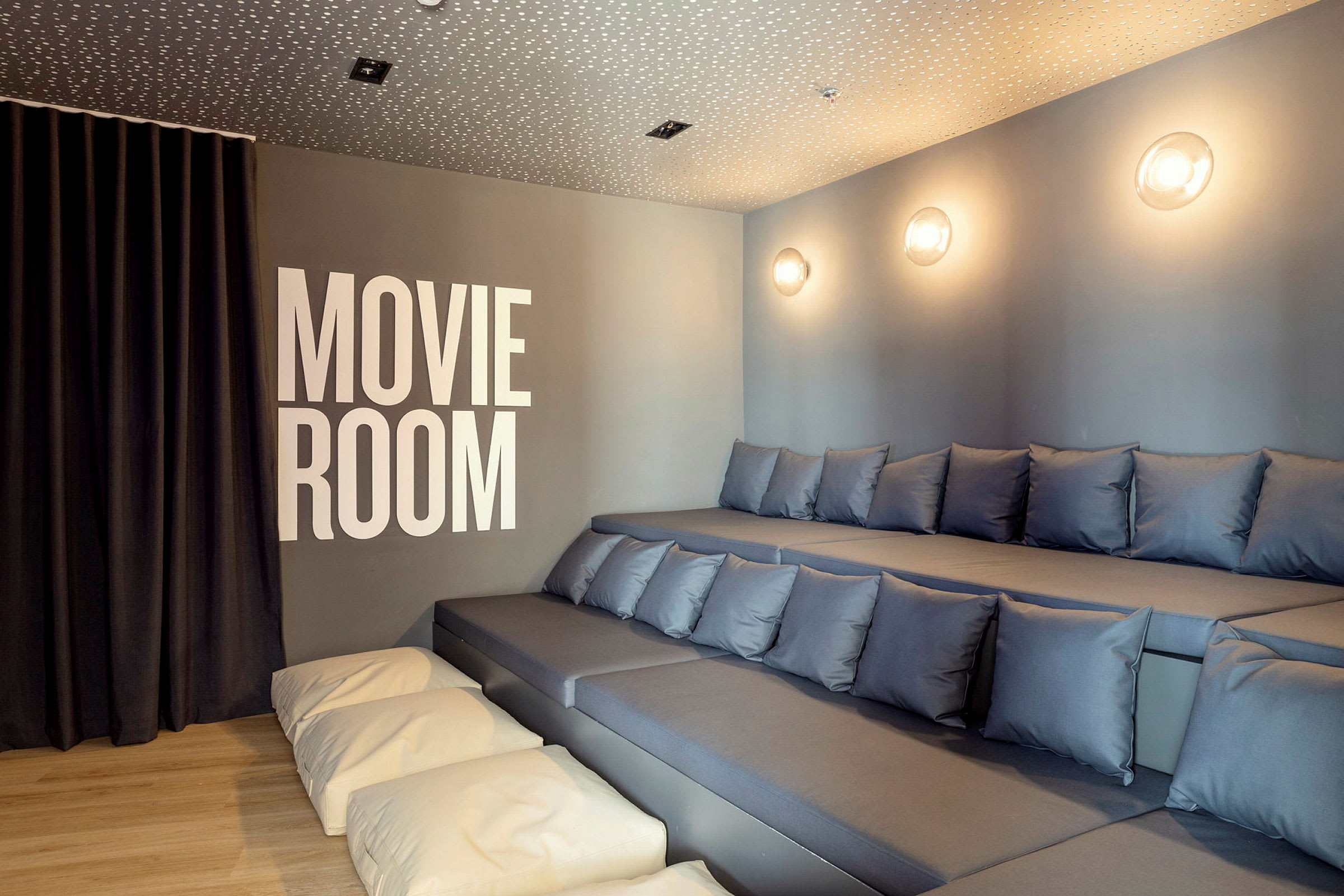 Bilder av ett rum för filmvisning med graderade sittplatser med kuddar och texten 'Movie Room' på väggen. (AI-genererad text)