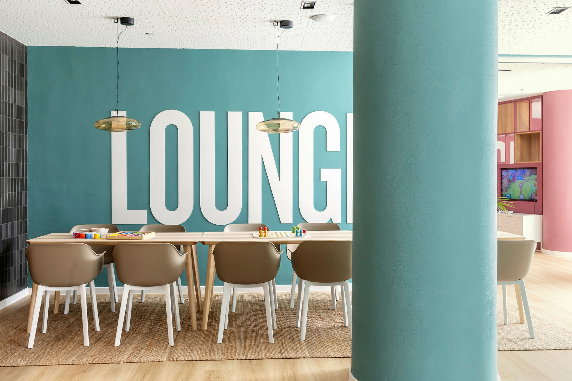 En bild på ett rum med en matta, stolar och ett bord framför en blå vägg med texten 'LOUNGE'. (AI-genererad text)