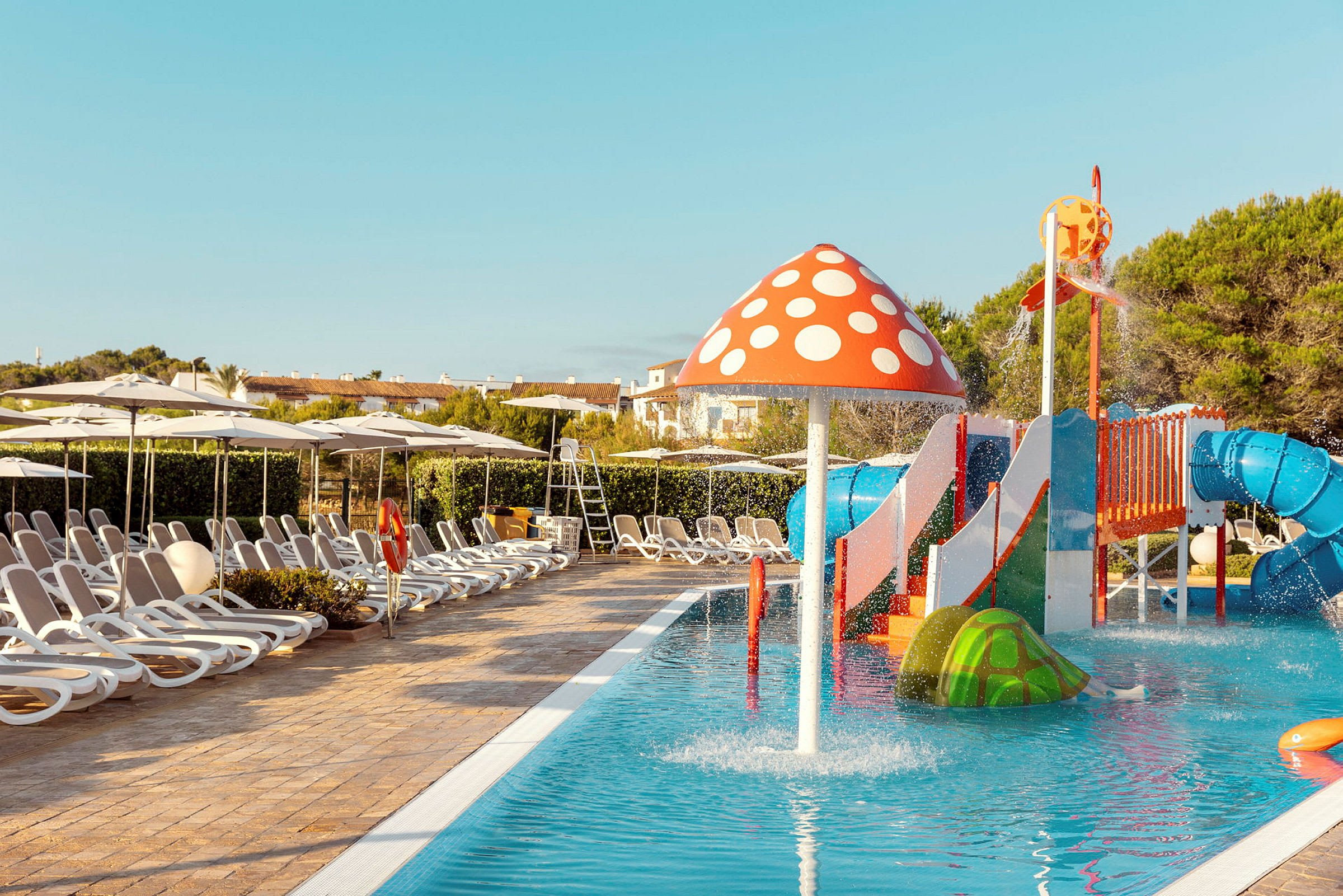 Pool med vattenlek för barn med färgglada figurer och solstolar runtom. (AI-genererad text)