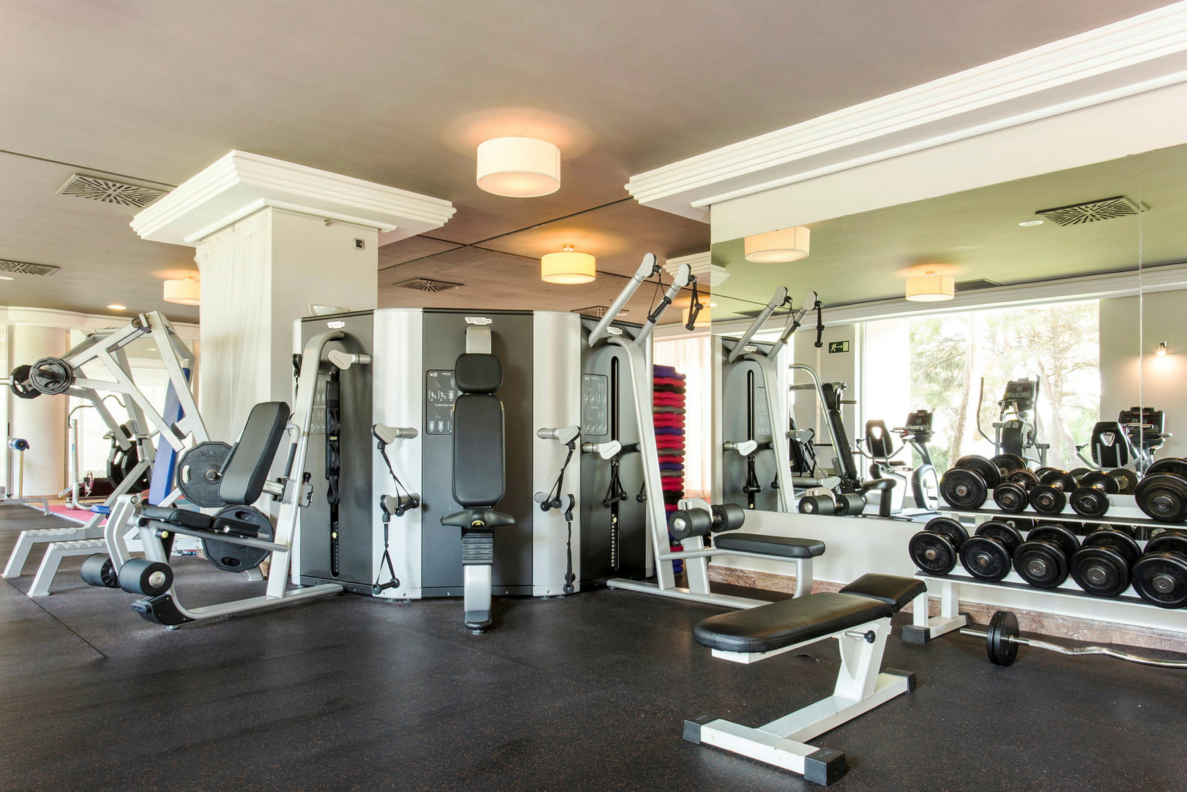 Ett gym med olika träningsmaskiner, hantlar och en spegel på väggen. (AI-genererad text)
