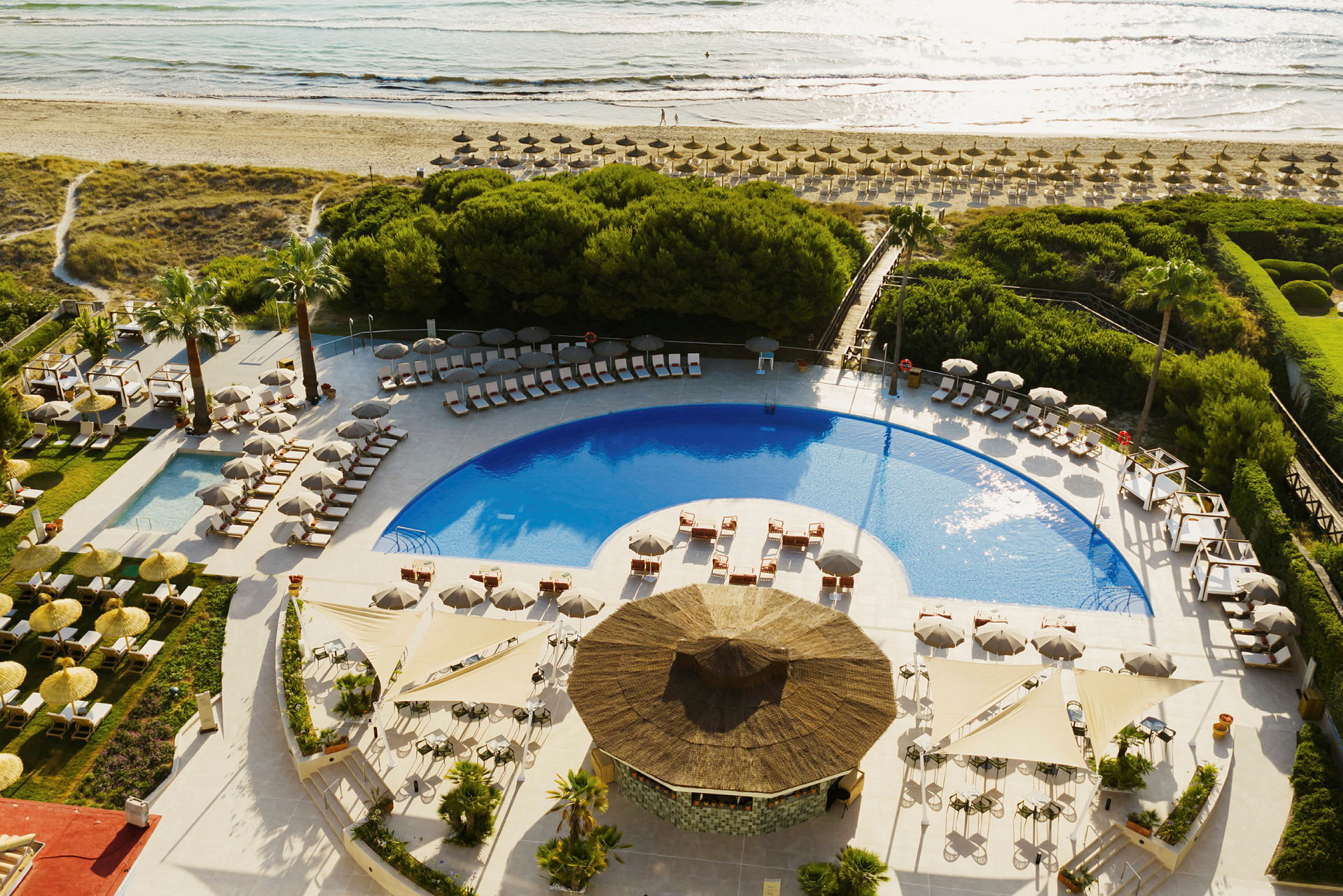 En pool omgiven av solstolar på ett hotellområde nära stranden. (AI-genererad text)
