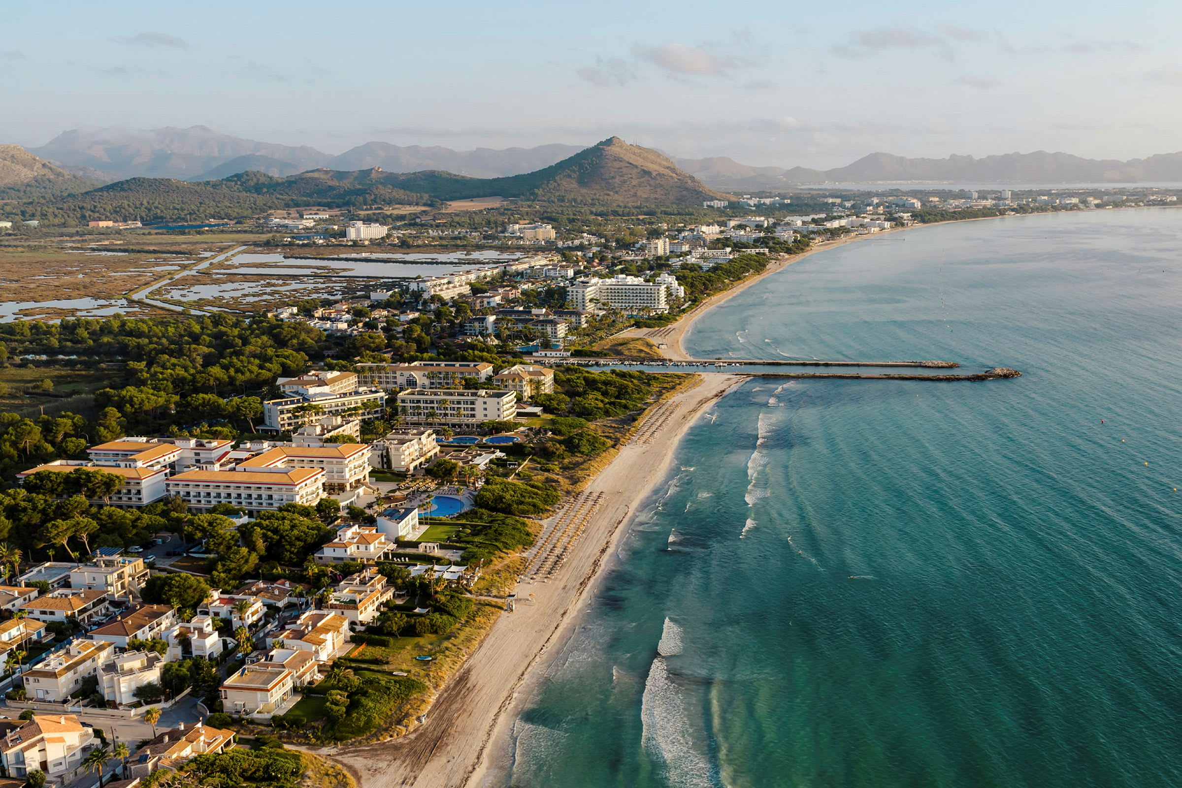 Utsikt över en kustlinje med en strand, hotellbyggnader och berg i bakgrunden. (AI-genererad text)