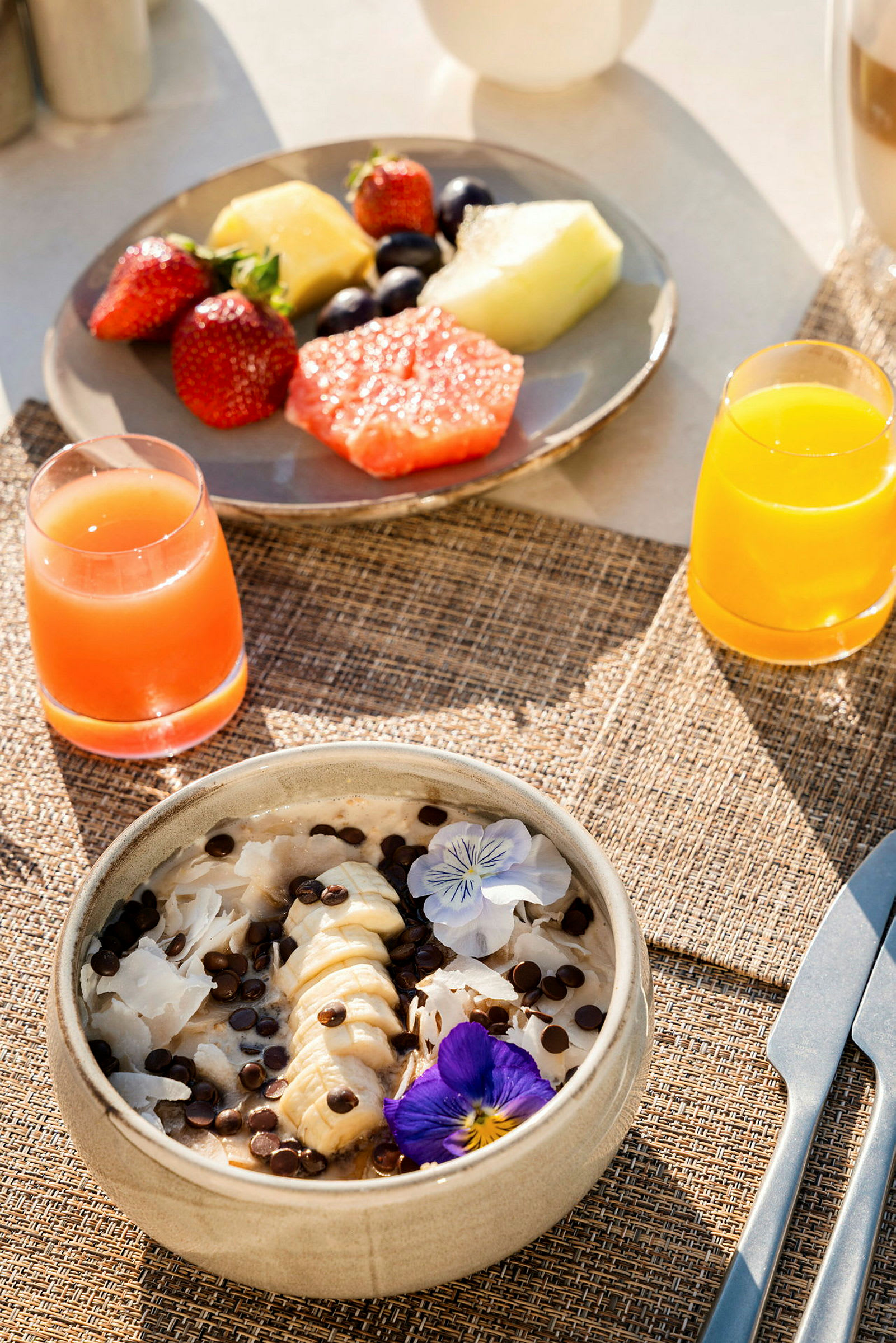 Frukostbord med färsk frukt, ett grynskål med bananskivor och chokladbitar, samt juice. (AI-genererad text)