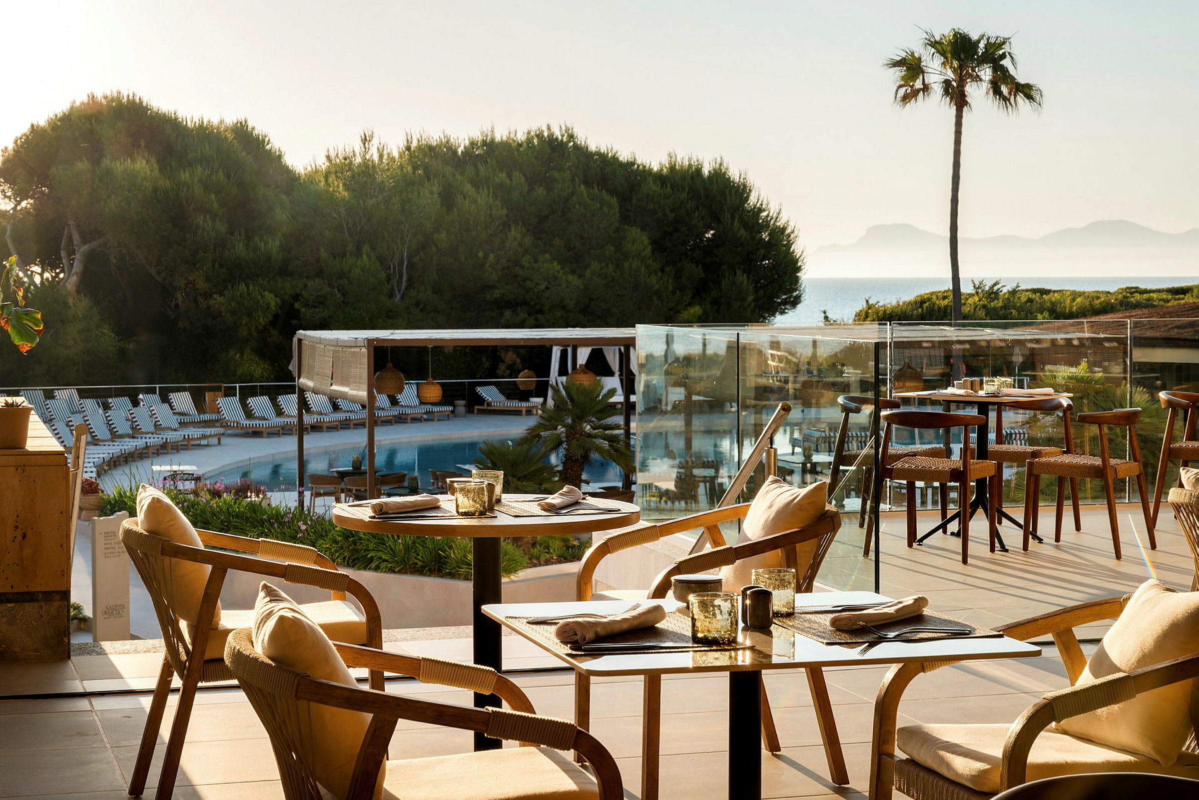Ett bord vid en utomhusrestaurang med utsikt över en pool, träd och havet i bakgrunden. (AI-genererad text)