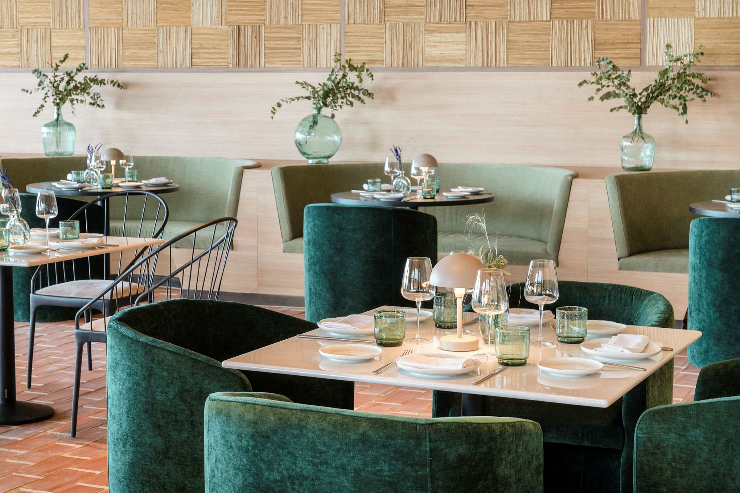 Ett elegant inrett restaurangområde med grön stoppning, dukade bord och dekorativa vaser med växter. (AI-genererad text)
