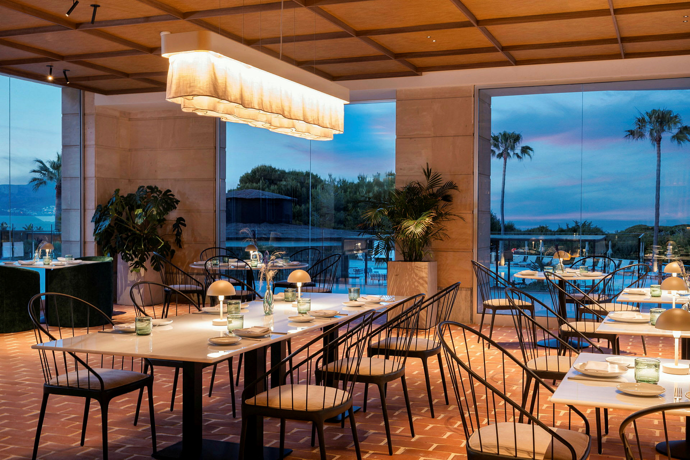 En elegant inredd restaurang med bord och stolar samt en ljus inredning. I bakgrunden syns stora fönster som visar en naturskön utsikt. (AI-genererad text)