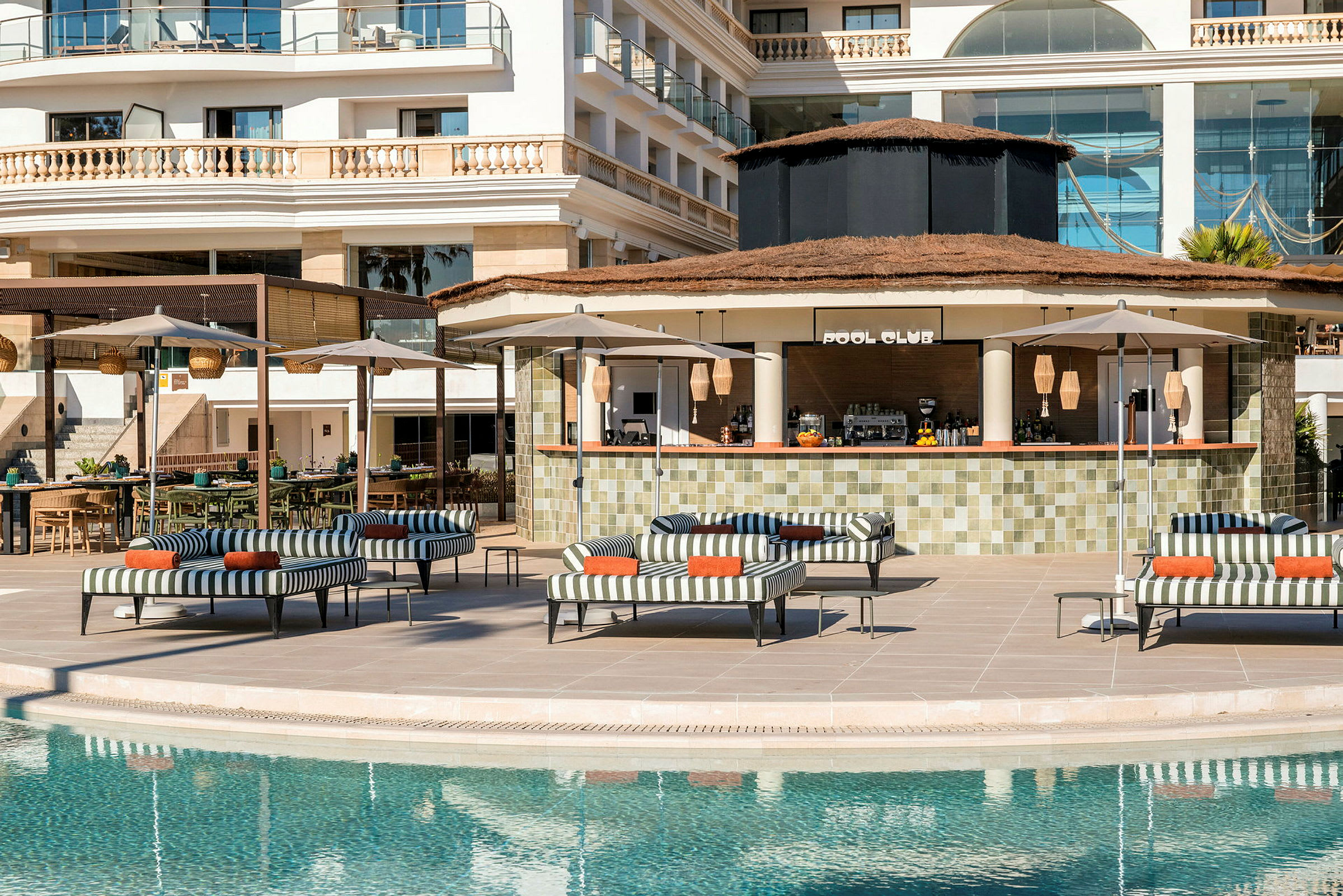En pool med solstolar, parasoller och en bar med skylt "Pool Club" i bakgrunden. (AI-genererad text)