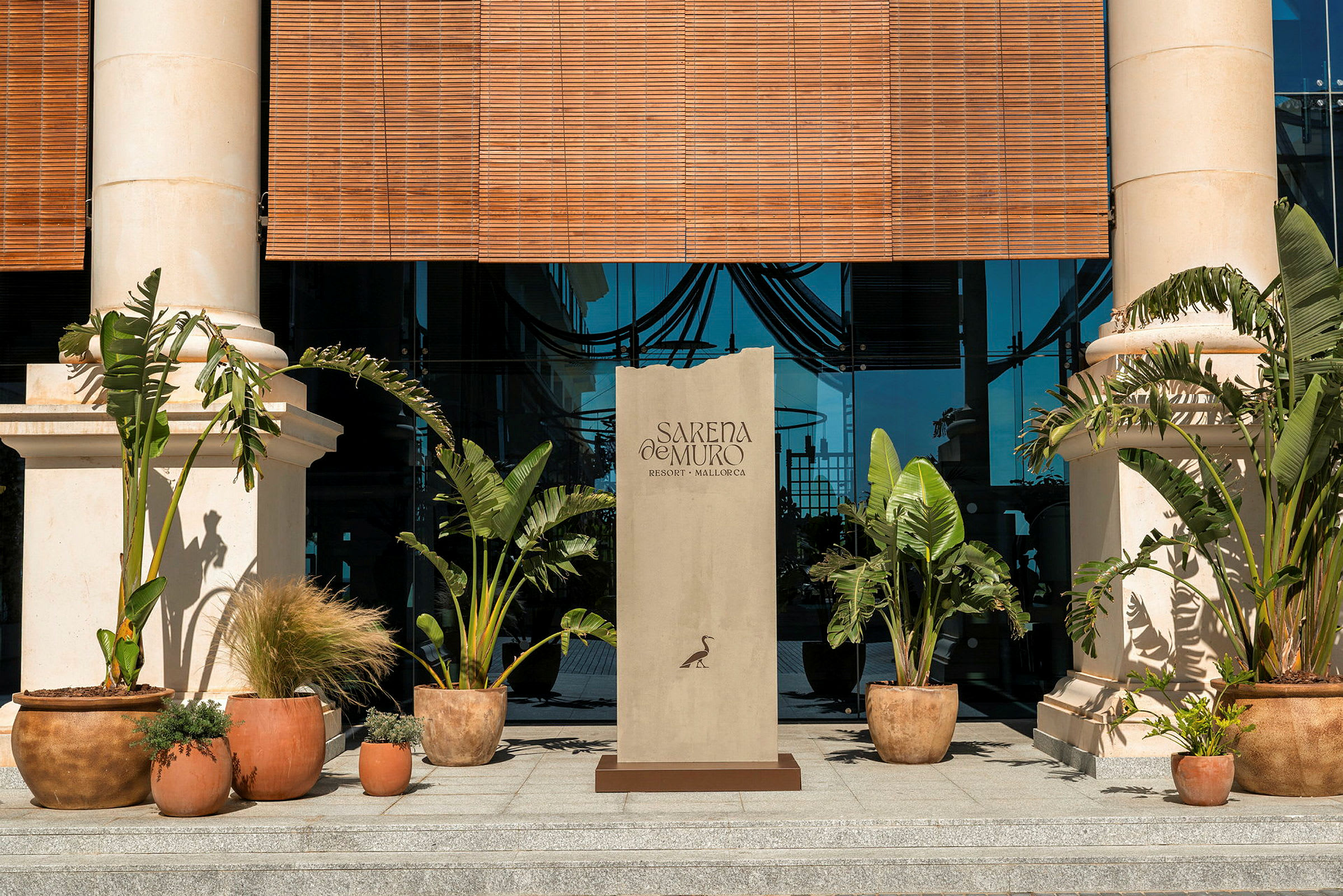 Ingången till en byggnad med två pelare, gröna växter i krukor och en skylt med texten "Sarena de Muro Resort Mallorca". (AI-genererad text)