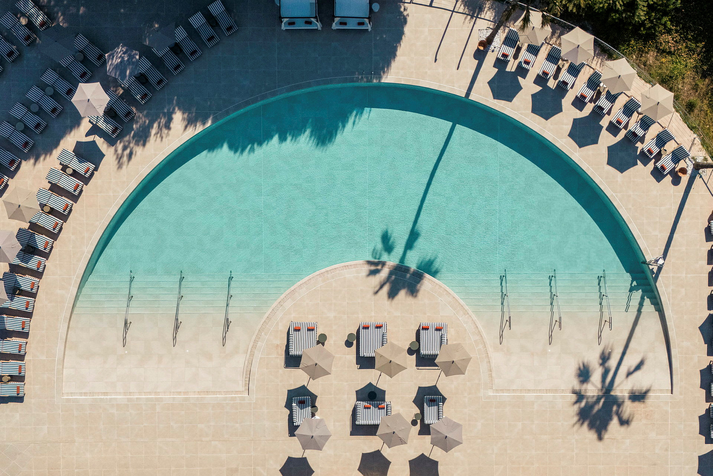 En ovanifrånbild av en pool med omgivande solstolar och parasoller. (AI-genererad text)