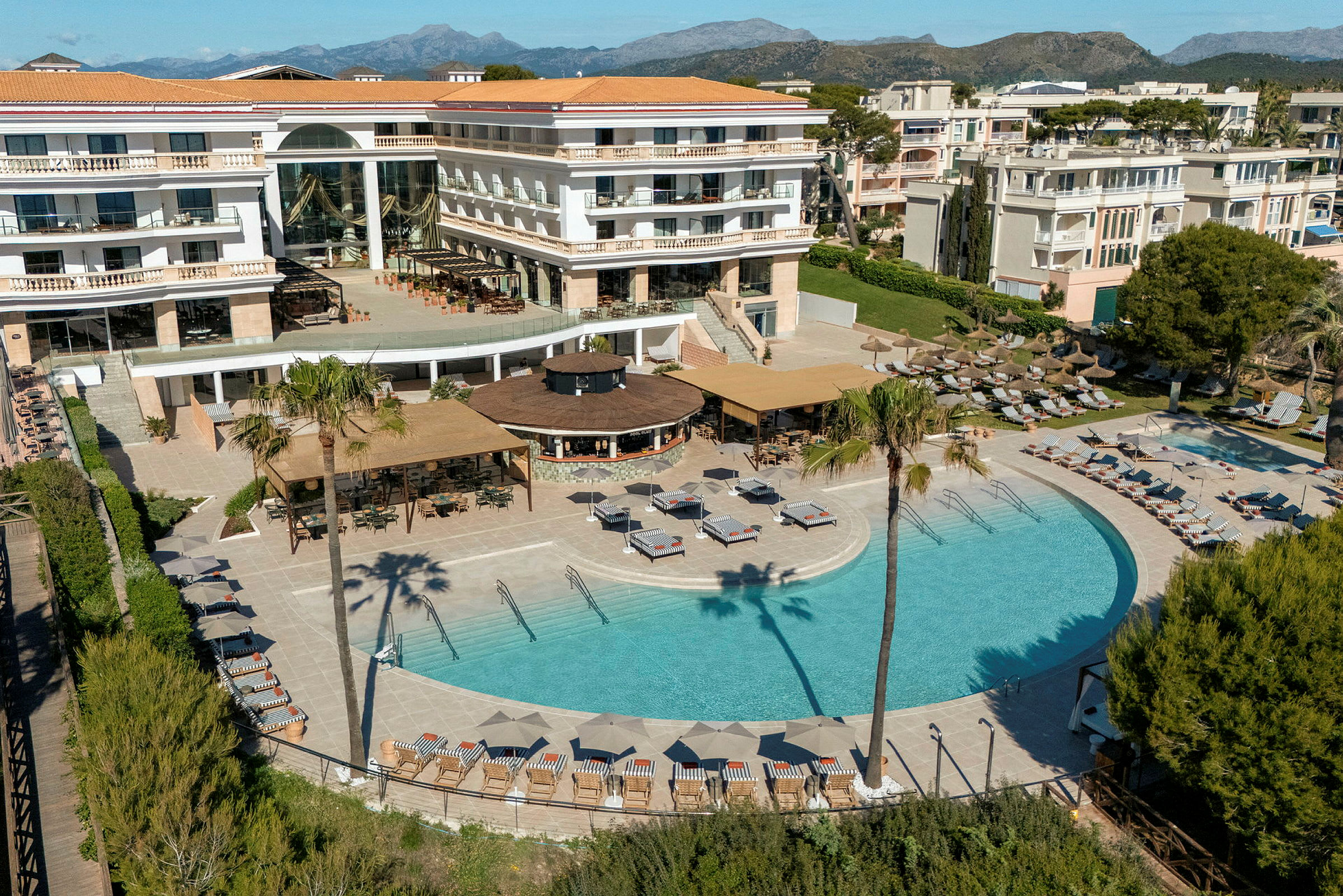 Hotell med pool- och terrassområde omgivet av solstolar, parasoller och grönska. (AI-genererad text)