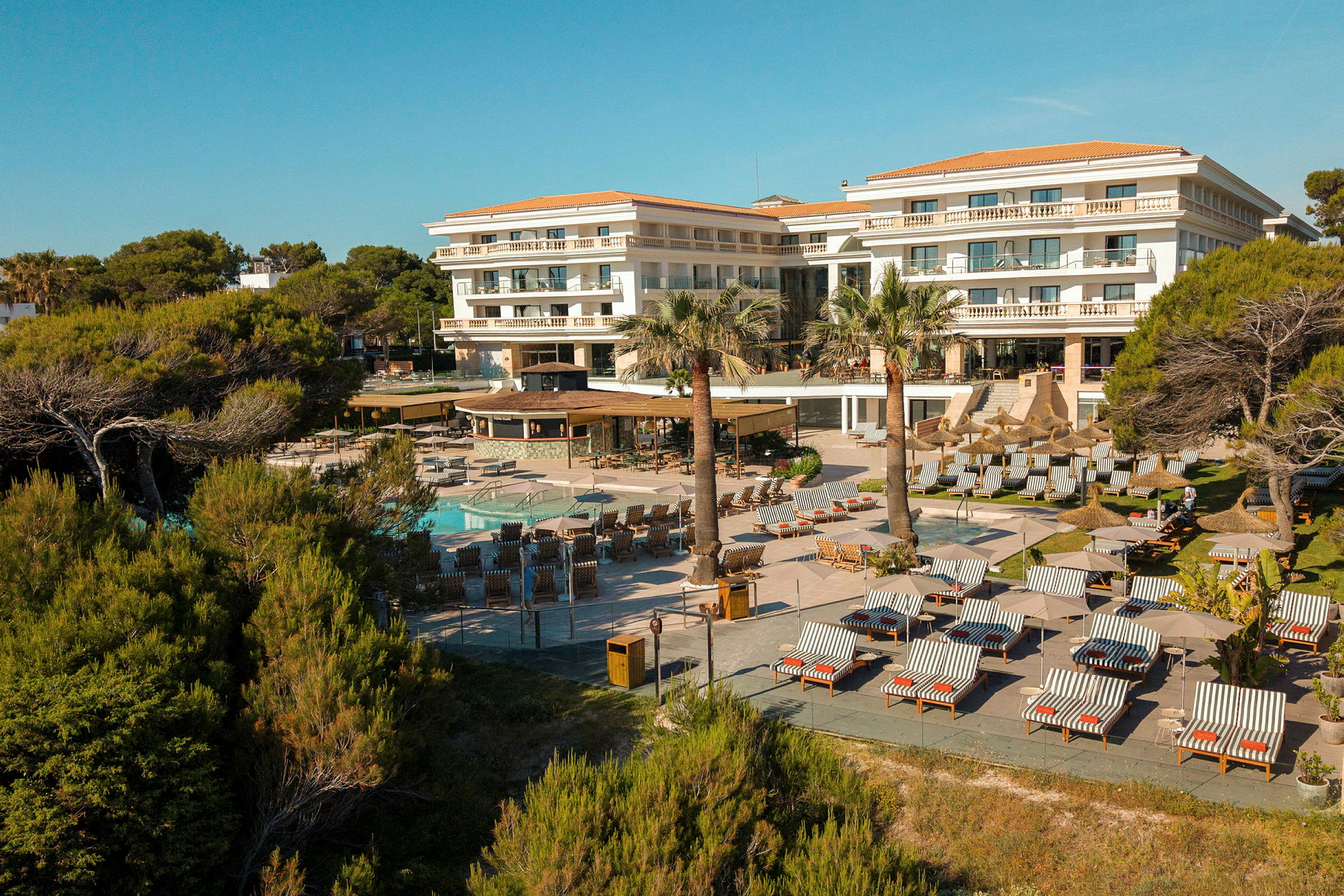 Ett hotell med poolområde och solstolar omgivet av träd och grönska. (AI-genererad text)