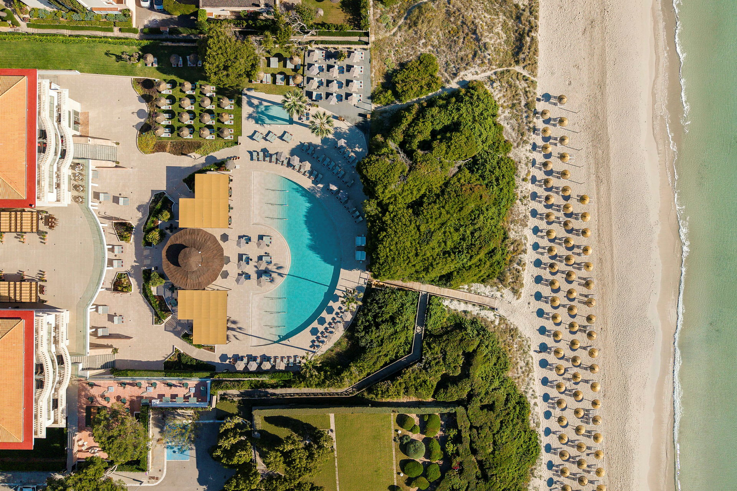 Flygbild av ett hotellområde med pool, grönområden, en strand och parasoll. (AI-genererad text)