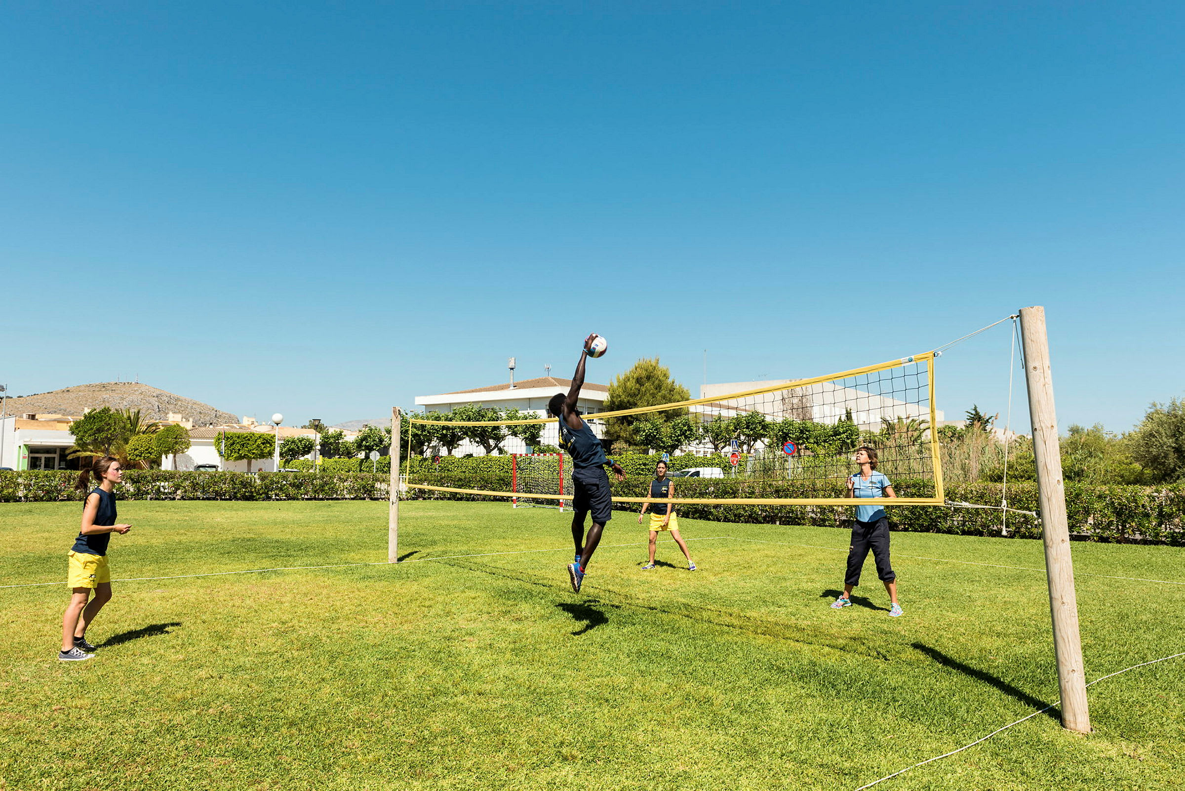 Personer spelar volleyboll på en gräsmatta under en klarblå himmel. (AI-genererad text)