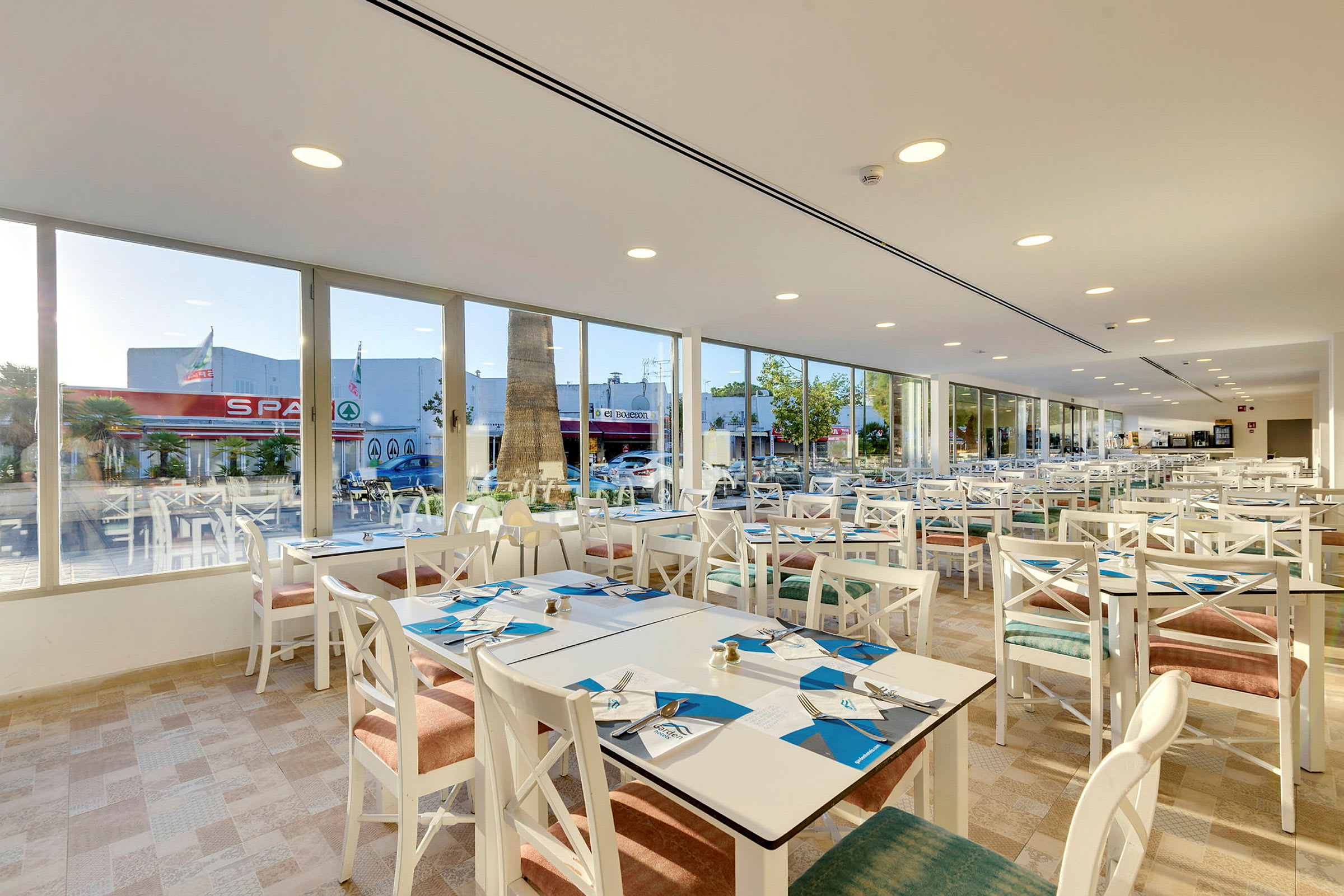Restaurang med vita möbler och fönster mot gatan. (AI-genererad text)