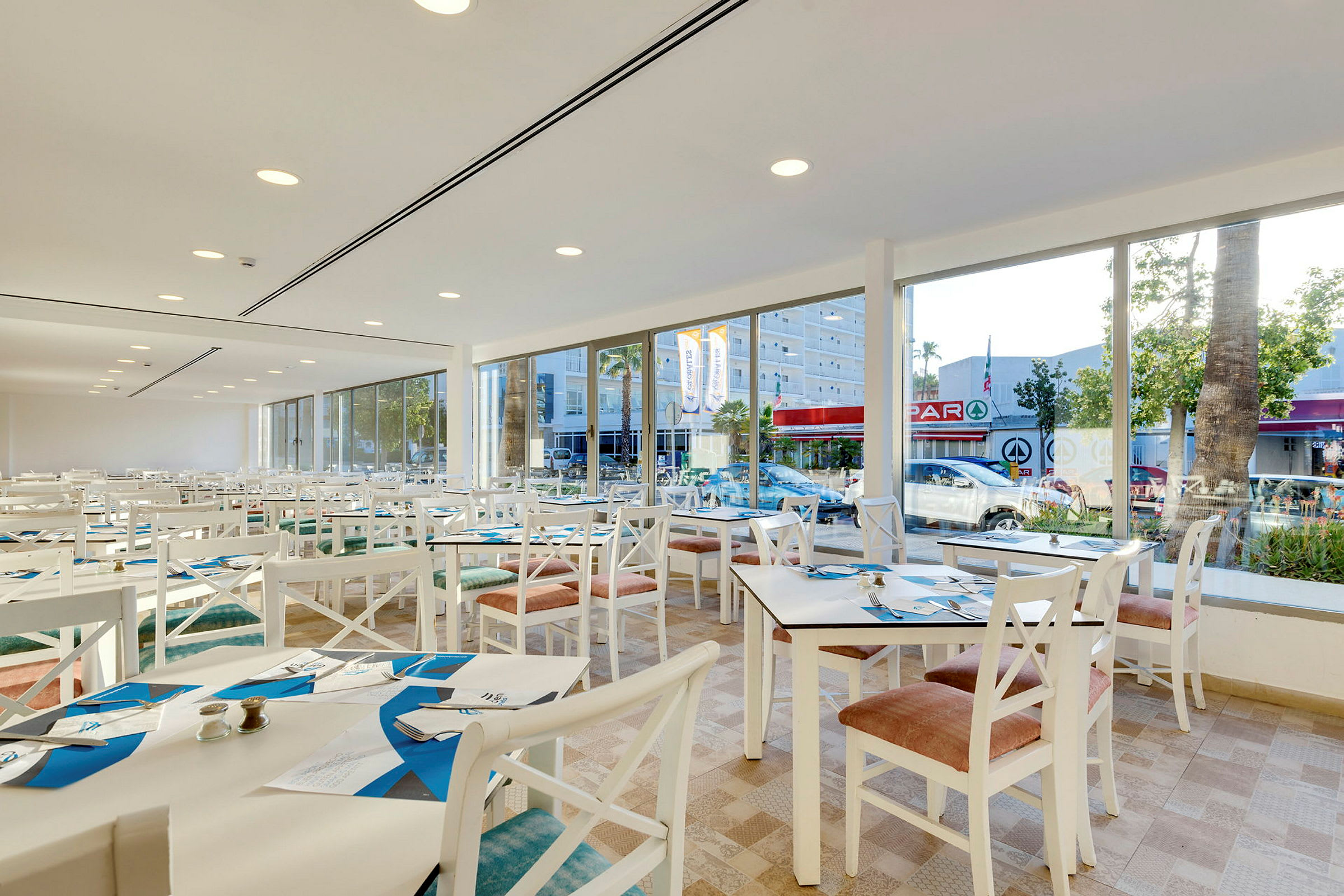 En rymlig restaurang med vita bord och stolar med stora fönster och utsikt mot gatan. (AI-genererad text)
