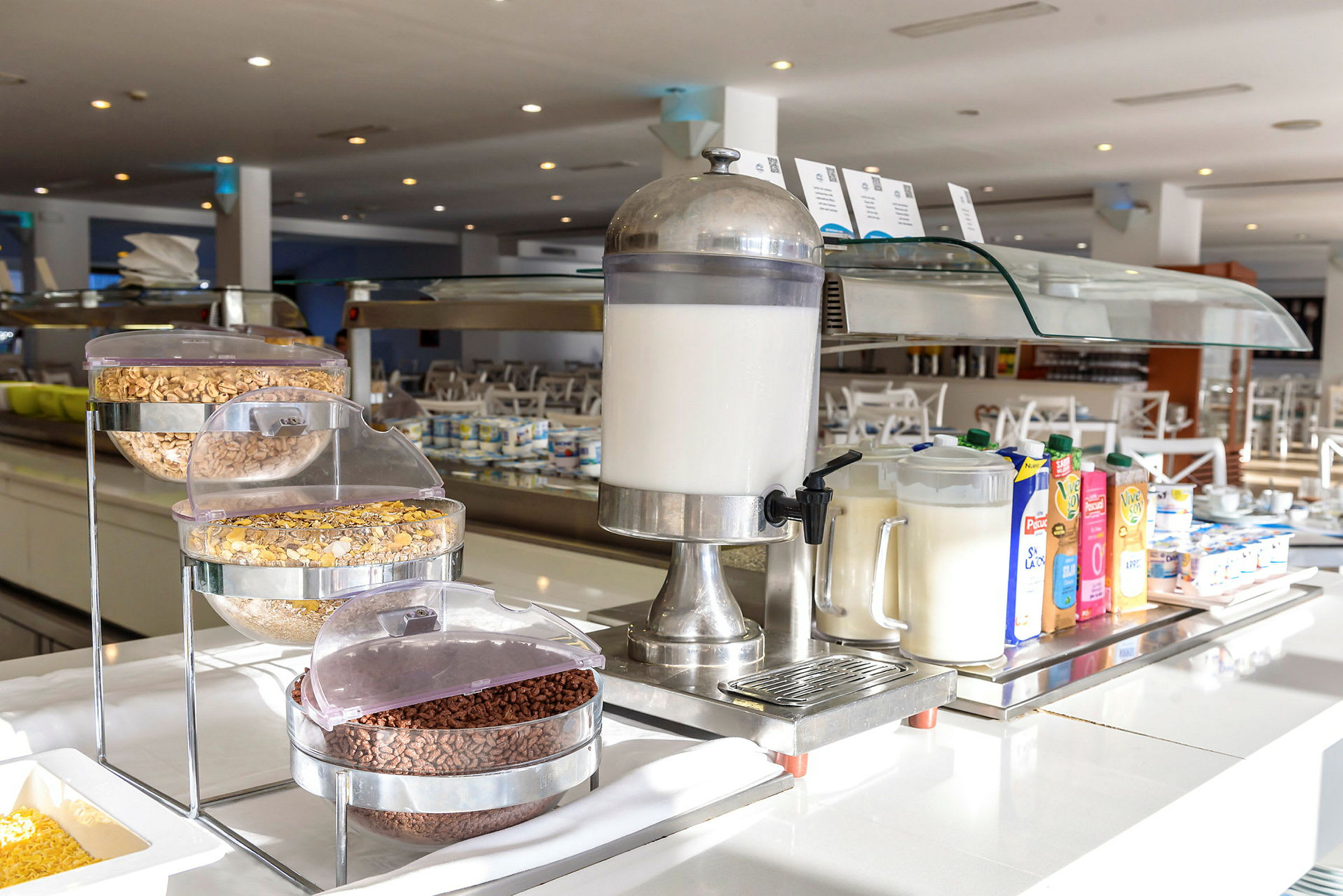 Bild av en hotellfrukostbuffé med mjölkautomat, spannmål och juiceförpackningar. (AI-genererad text)