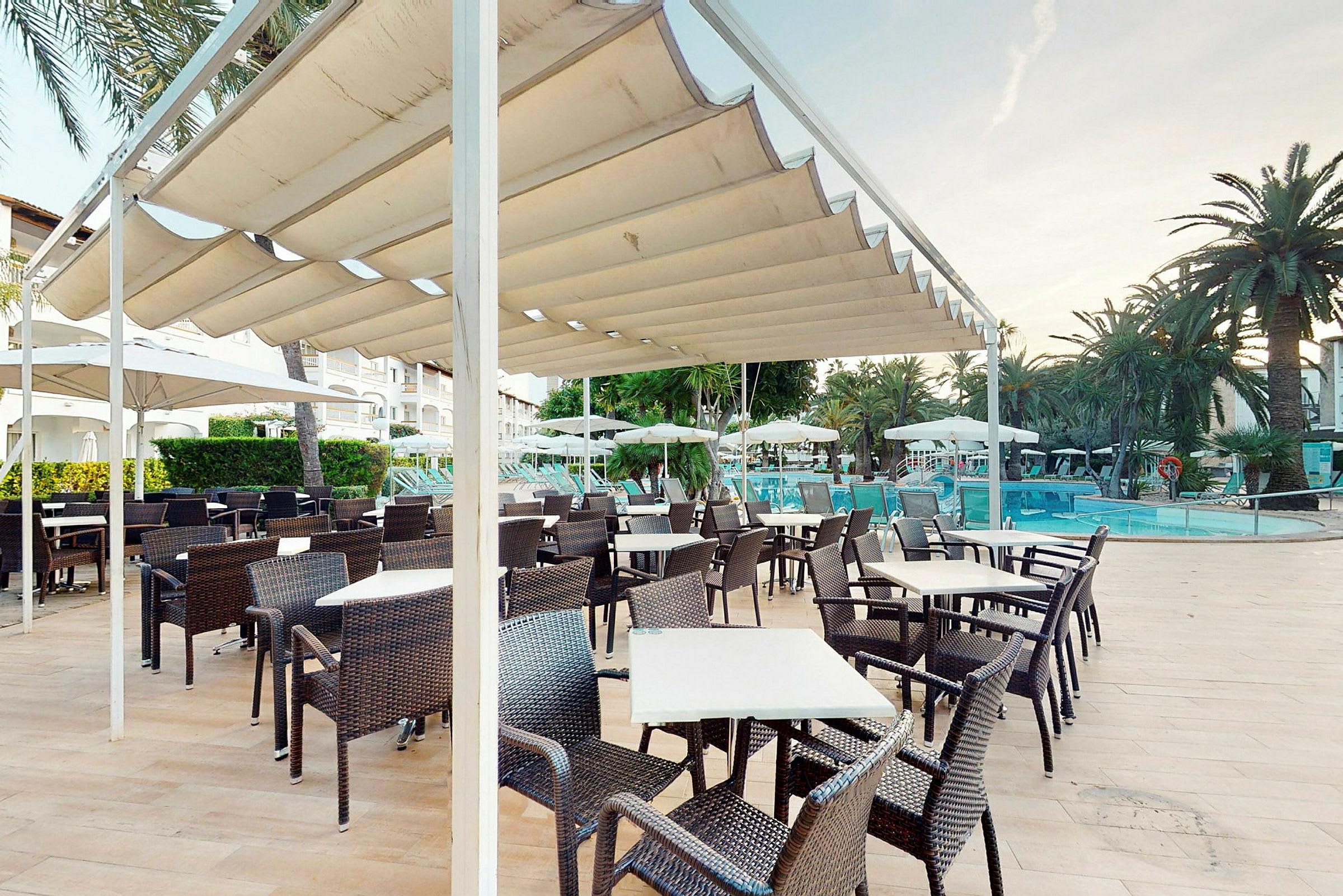 En uteservering med bord och stolar under en pergola nära en pool. (AI-genererad text)