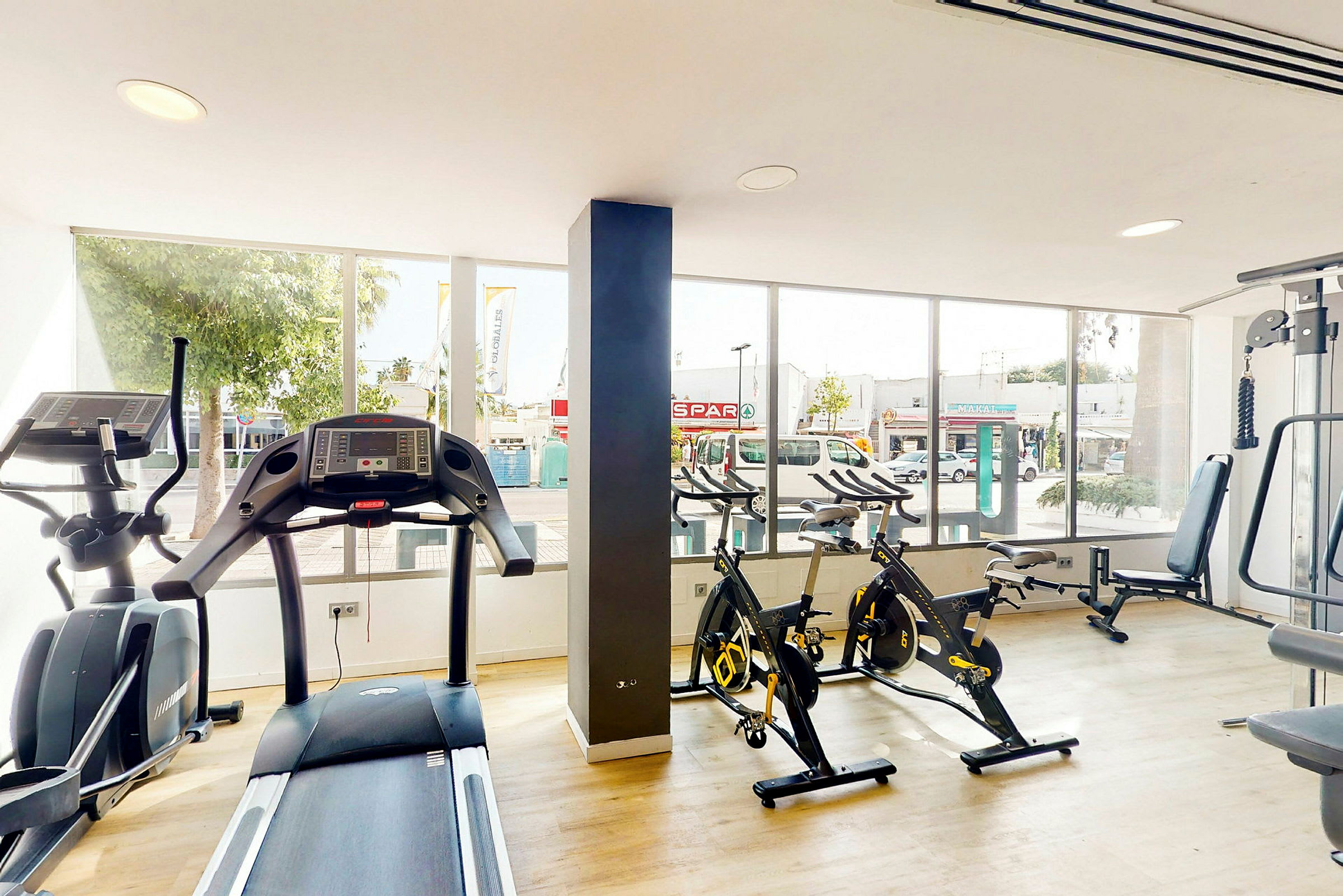 Ett gym med träningsmaskiner inklusive löpband och motionscyklar framför stora fönster. (AI-genererad text)