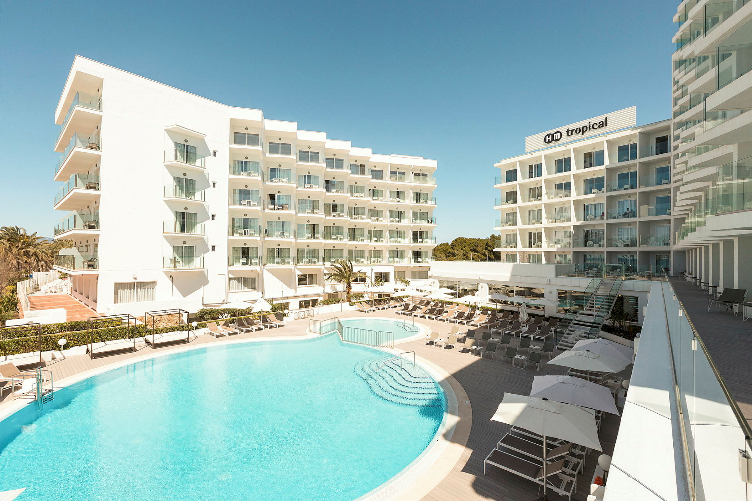 Bild på hotellbyggnader med utomhuspool och solstolar. (AI-genererad text)