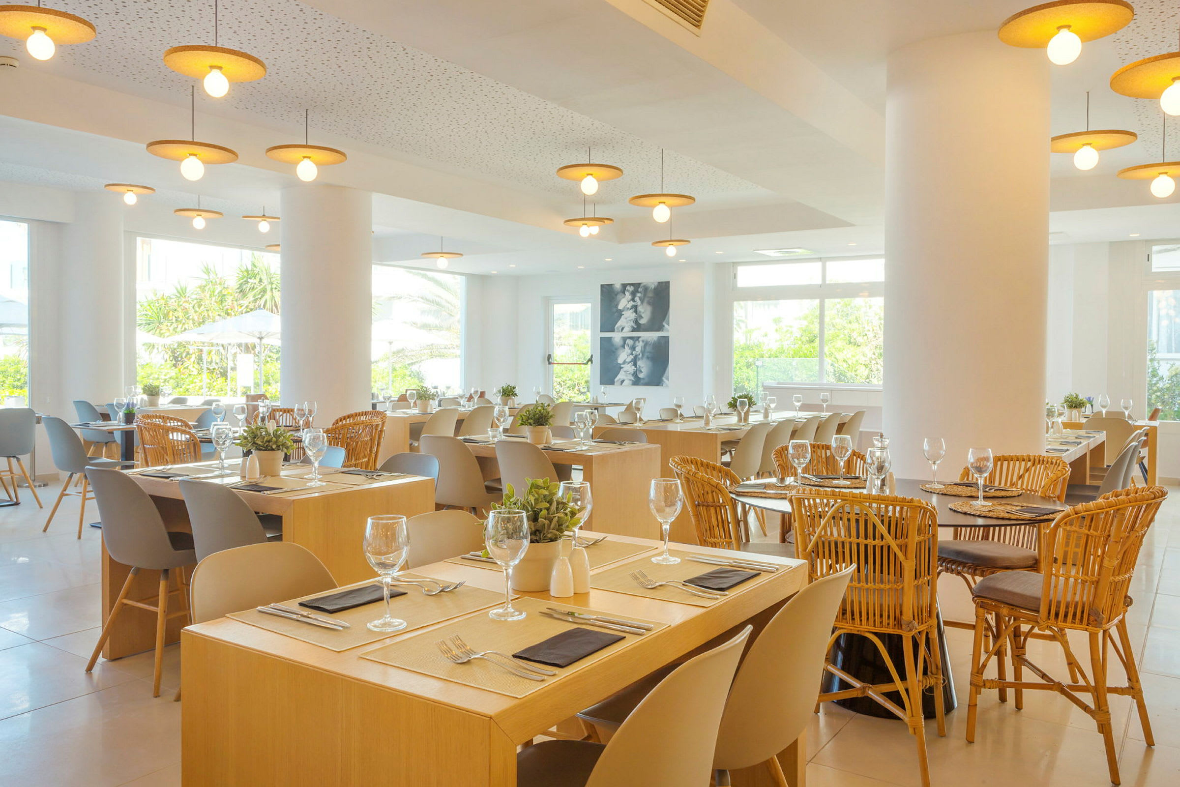 Ett ljust och luftigt restaurangrum med dukade bord och stolar. Fönstren släpper in naturligt ljus. (AI-genererad text)