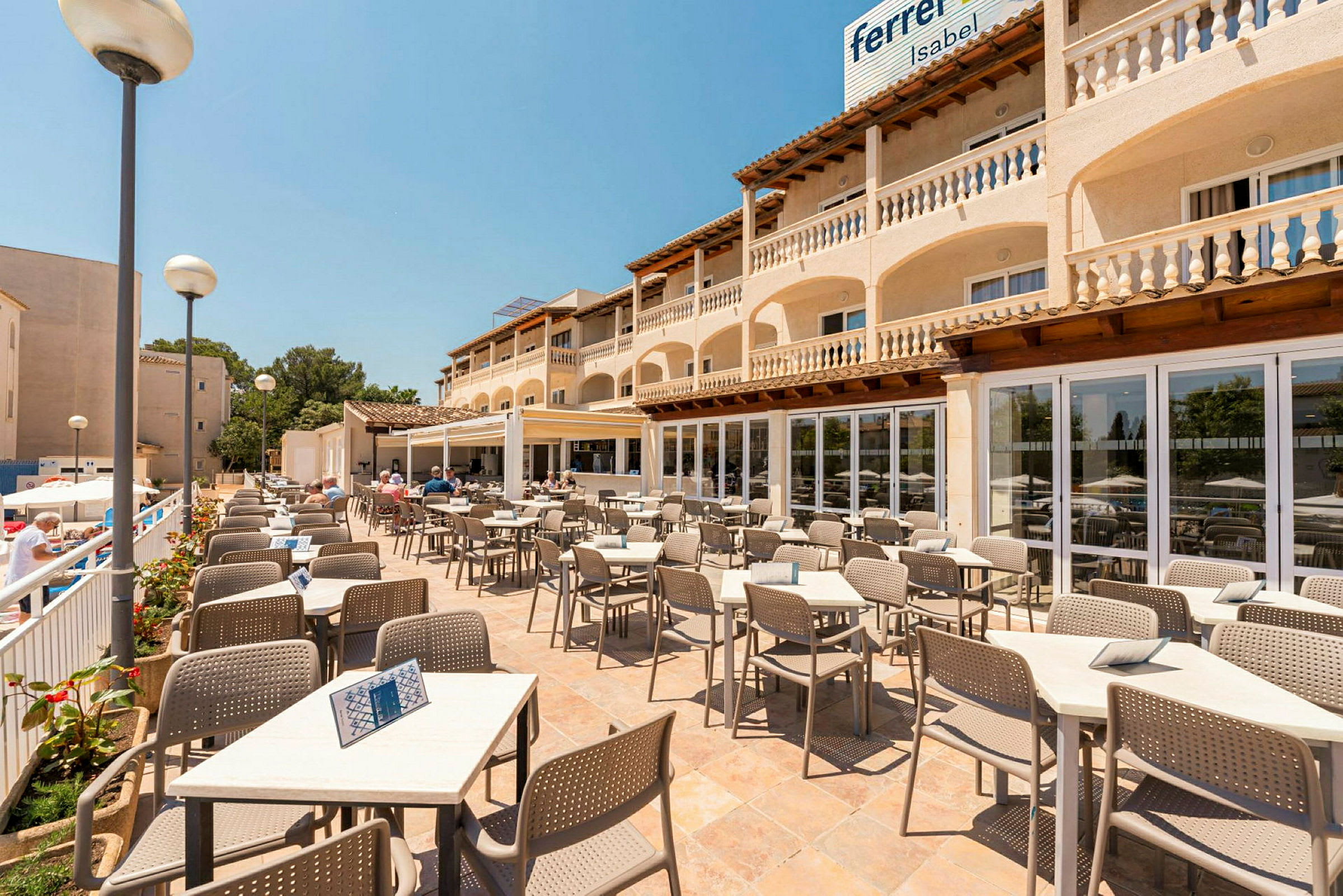 Terrassrestaurang med bord och stolar, omgiven av en byggnad med balkonger. (AI-genererad text)