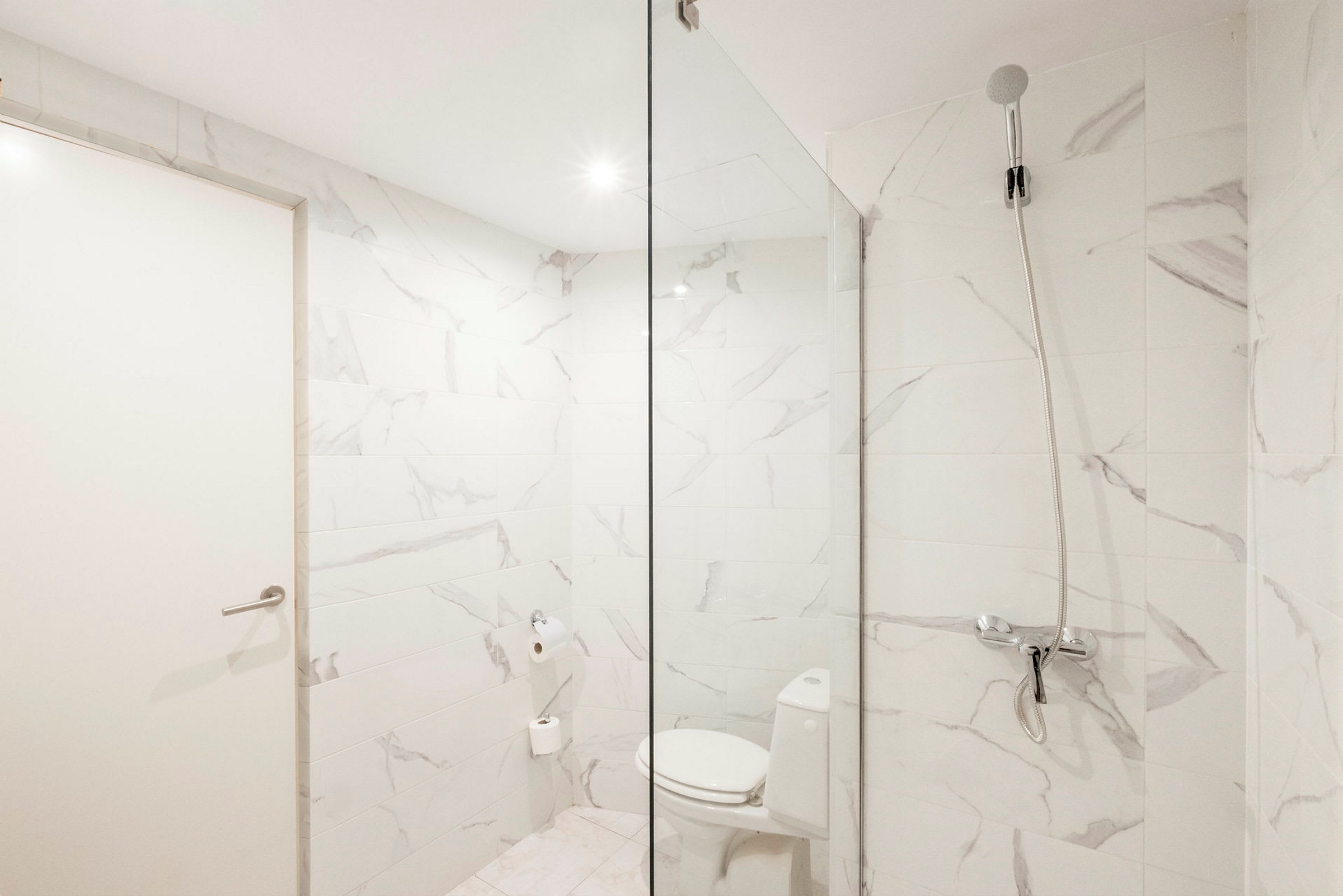 Ett badrum med vita marmorerade väggar, en toalettstol och en dusch med glasvägg. (AI-genererad text)