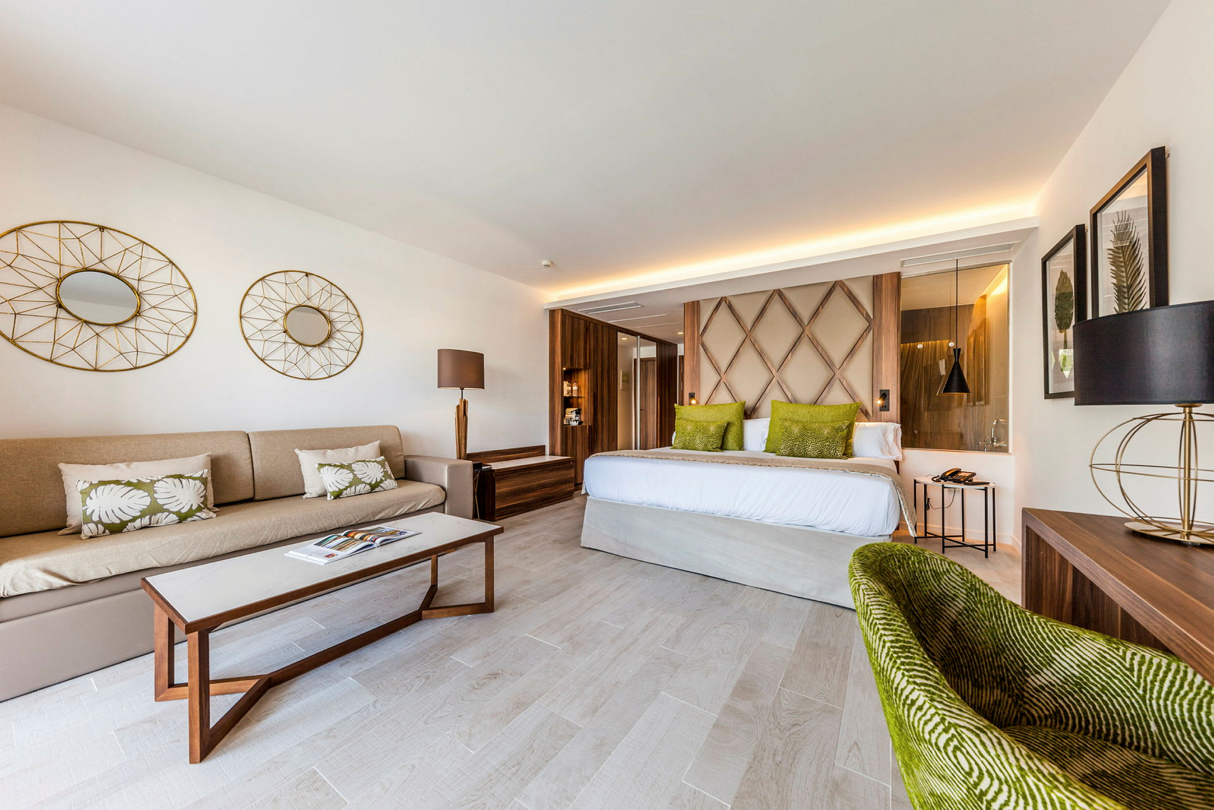 Ett hotellrum med modern inredning, inklusive en soffa, ett bord, en säng med gröna kuddar och dekorativa detaljer. (AI-genererad text)