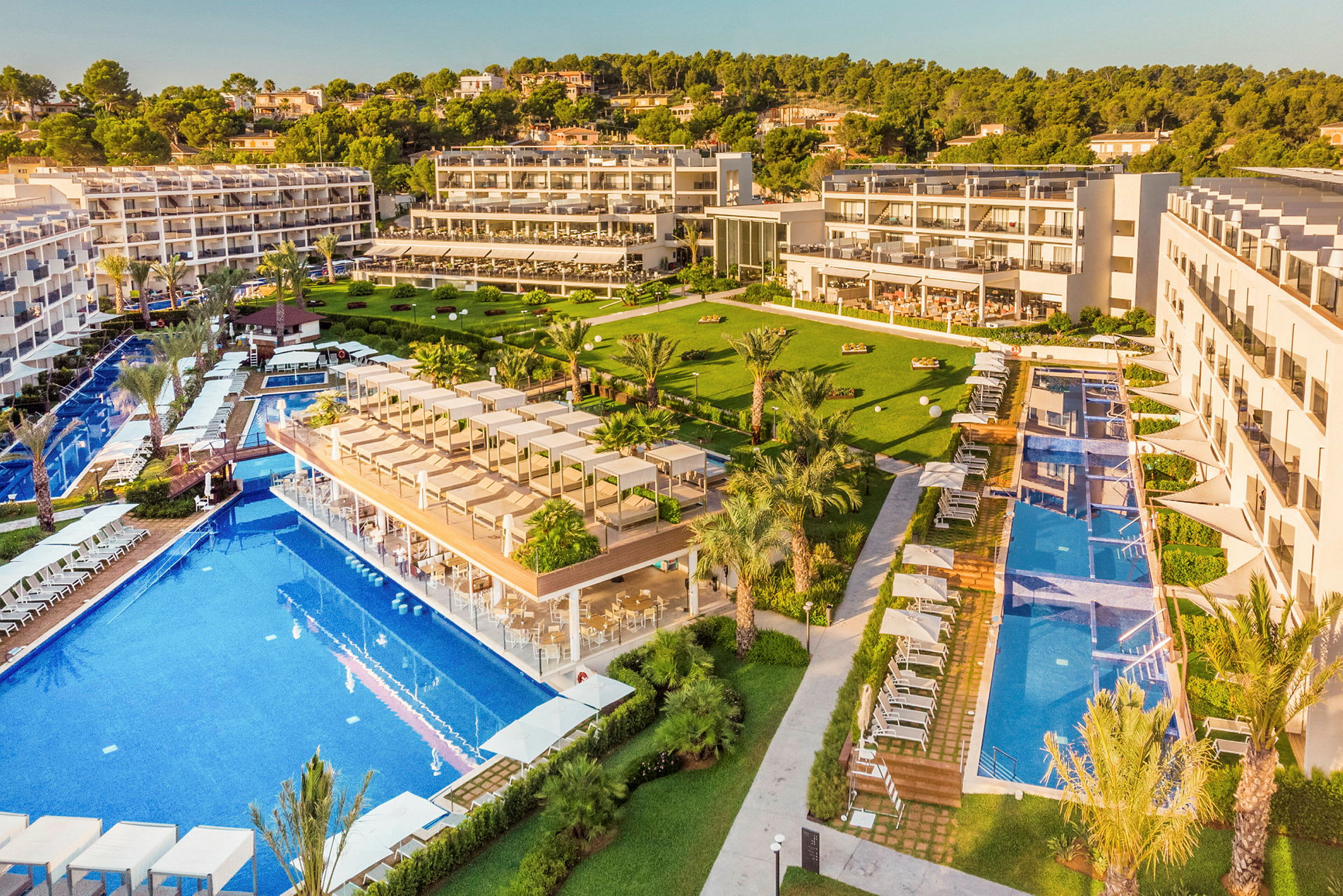 Flera hotellbyggnader med stora pooler och grönområden omgivna av träd. (AI-genererad text)