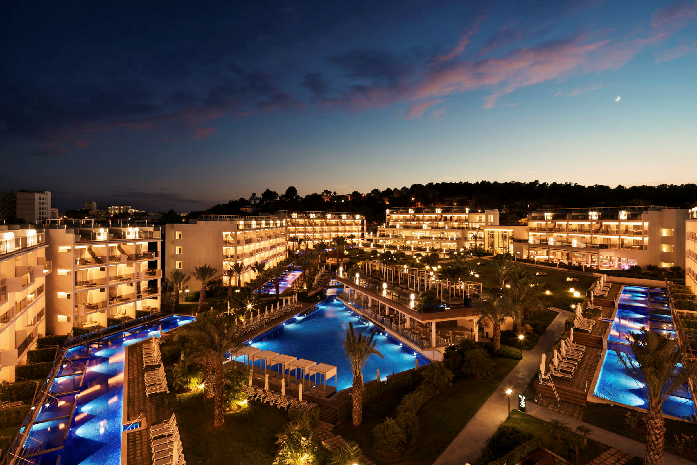 Vy över hotellkomplex på kvällen, med upplysta byggnader och pooler. (AI-genererad text)