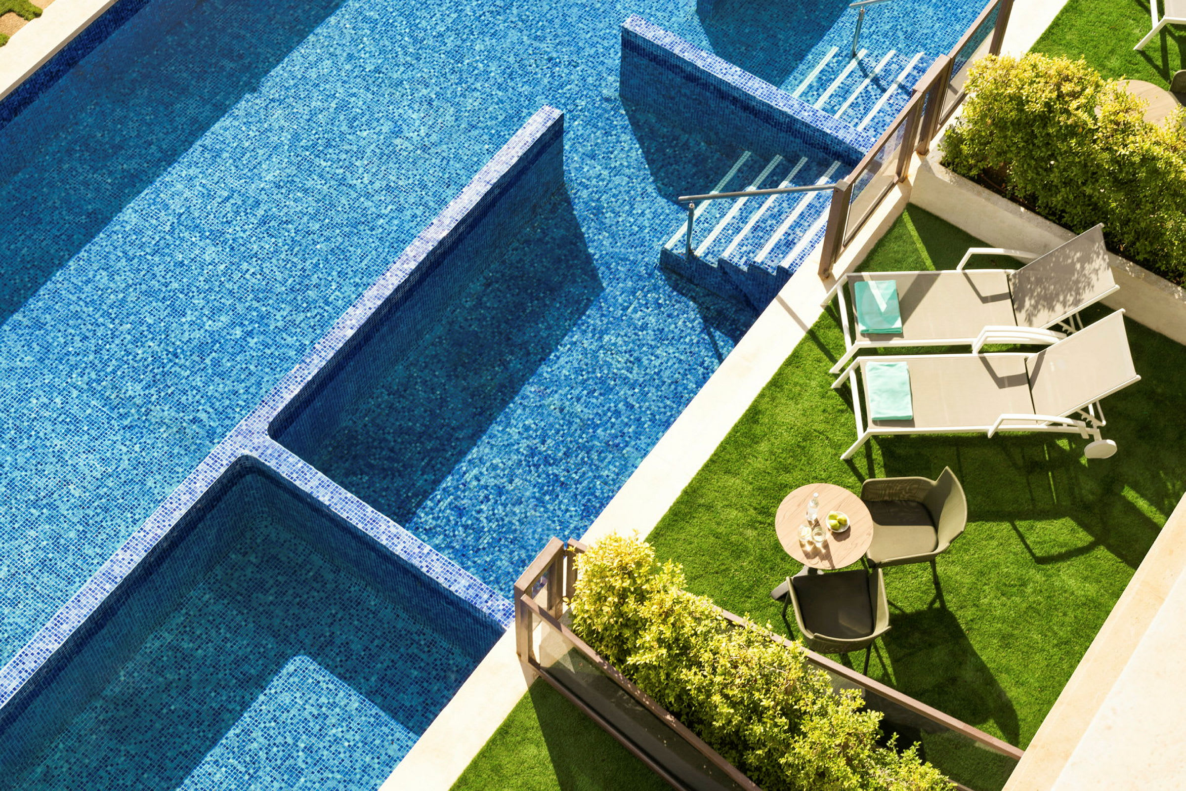 Bild av en swimmingpool med blå mosaik, två solstolar och ett bord med stolar på en grönyta. (AI-genererad text)