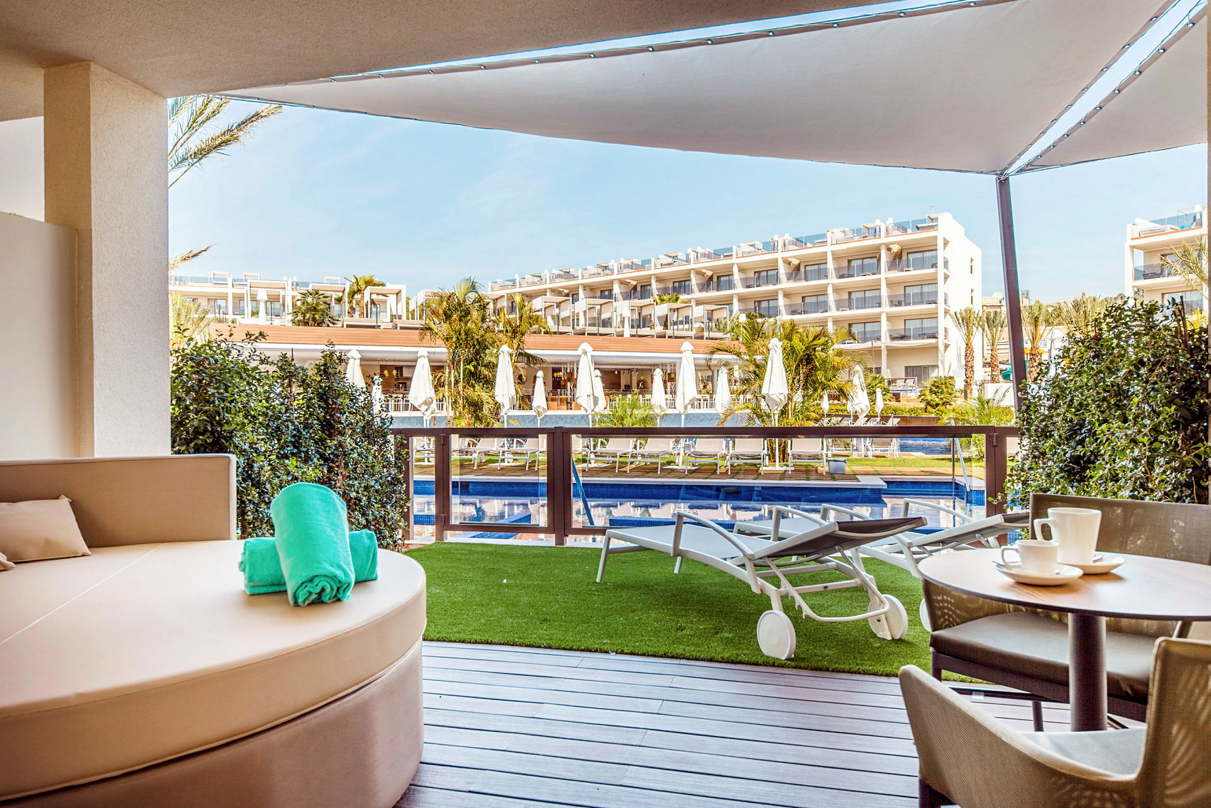 Vy från terrass med pool och solstolar framför hotellbyggnad. (AI-genererad text)