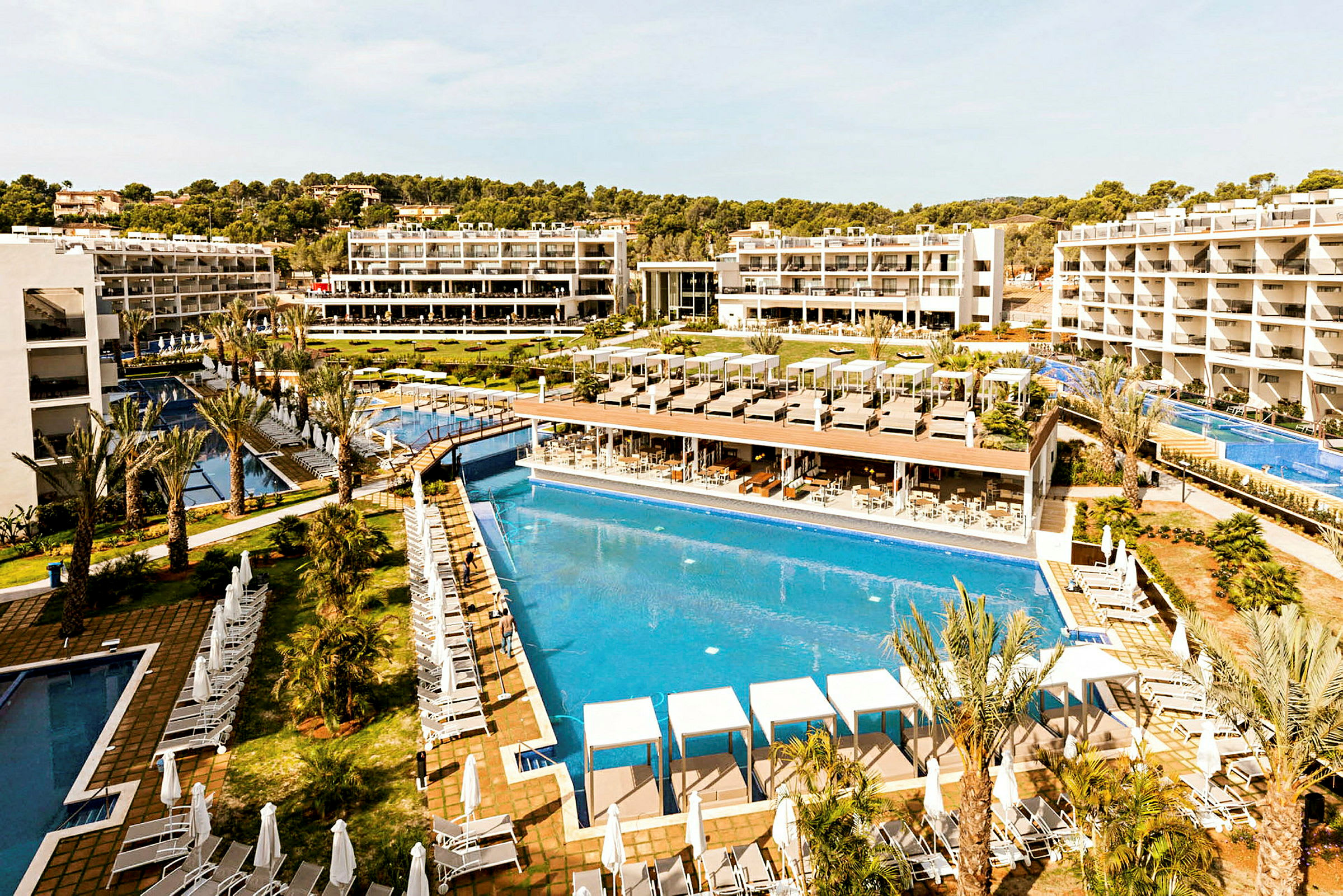 Ett semesterhotell med flera utepooler, solstolar och vita byggnader i bakgrunden. (AI-genererad text)